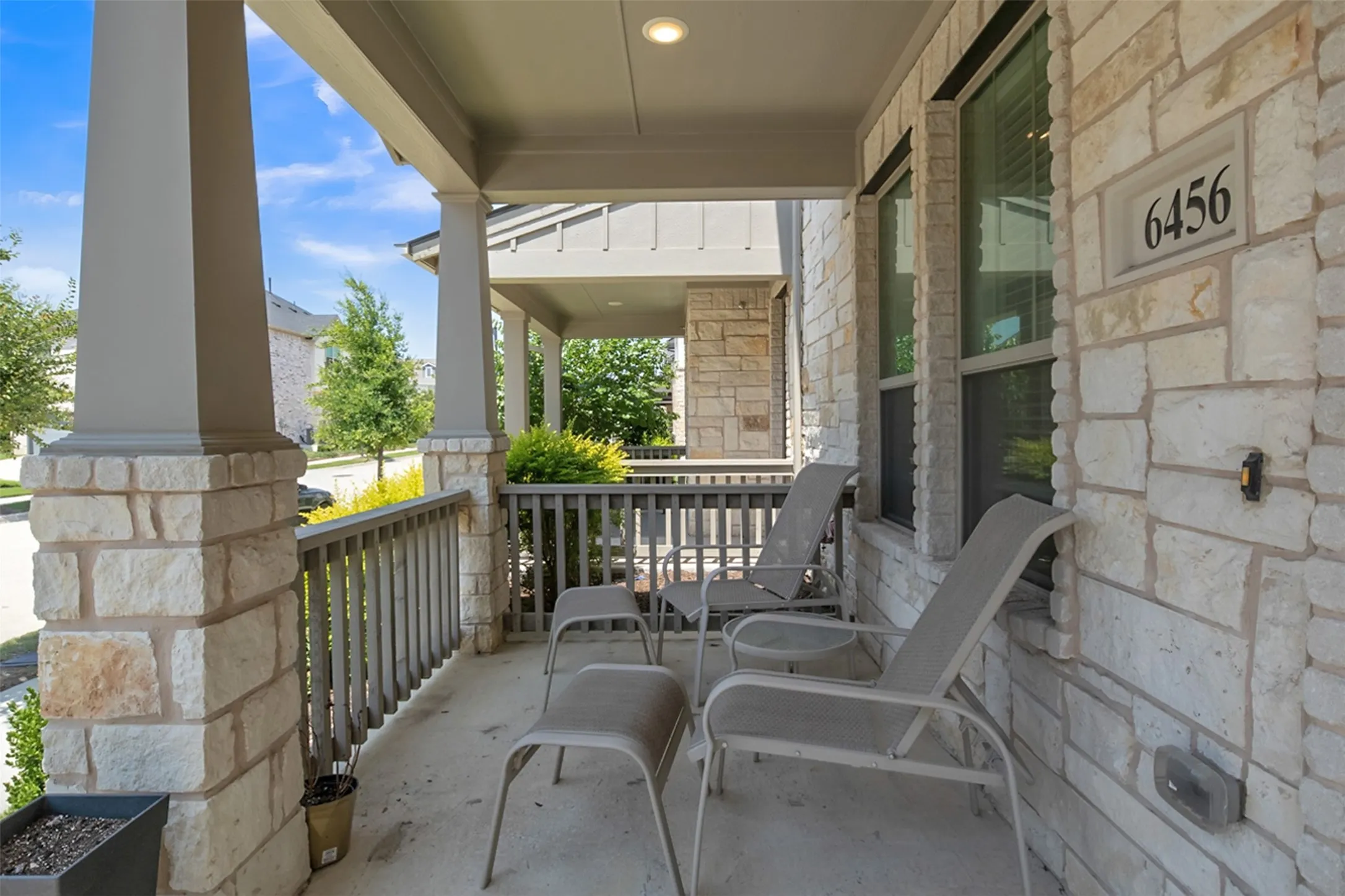Welcoming covered front porch featuring stone and brick exterior, metal railings, and multiple seating areas