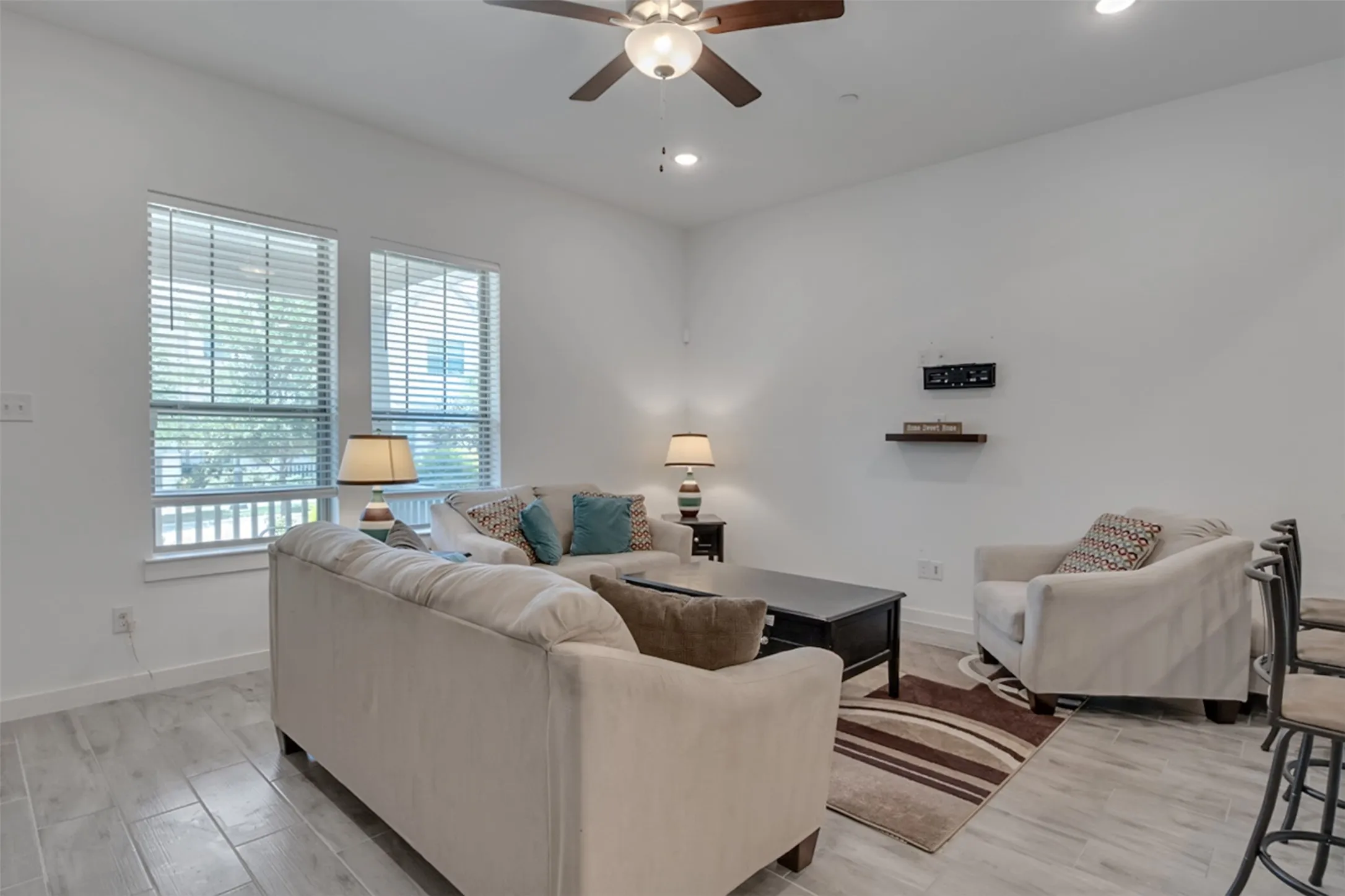 Recessed lighting, ceiling fan, two windows with blinds, wood-finish flooring, and a floating wall shelf