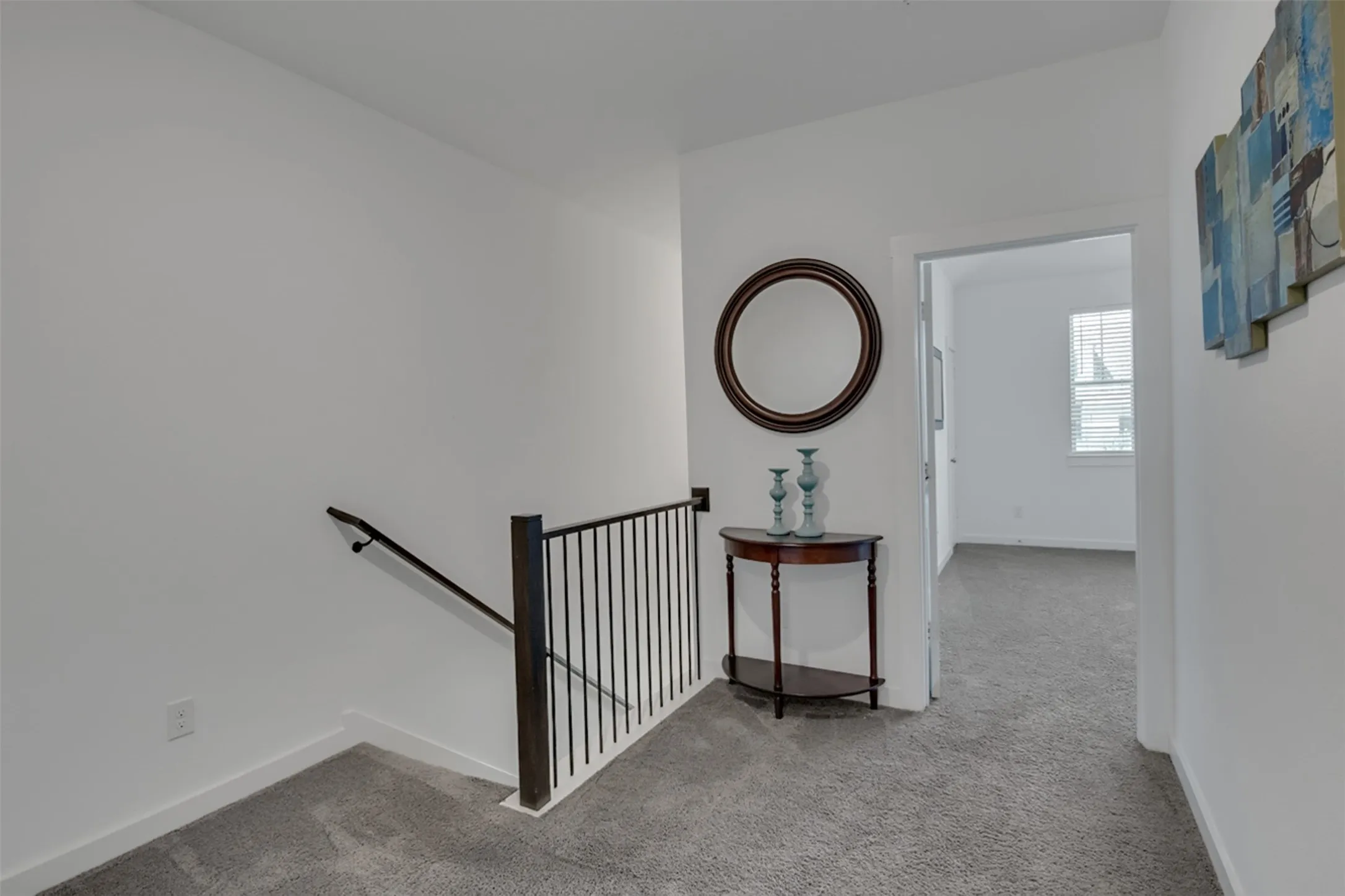 Carpeted hallway with white walls and a dark metal stair railing