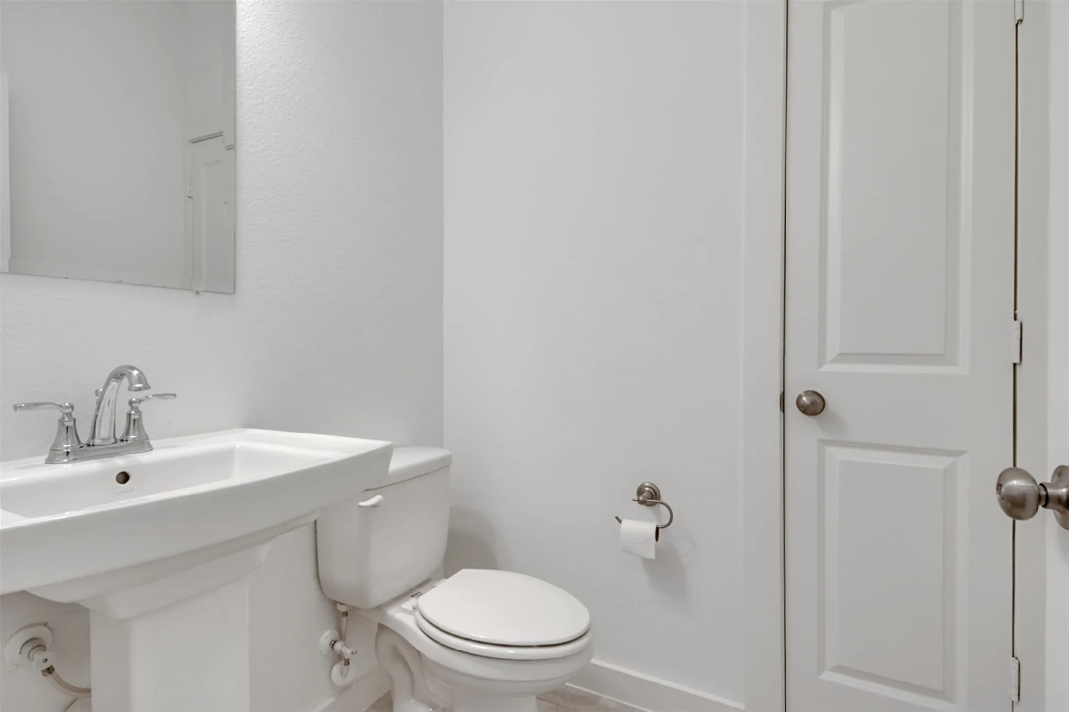 White pedestal sink with chrome faucet, white toilet, and white paneled interior doors