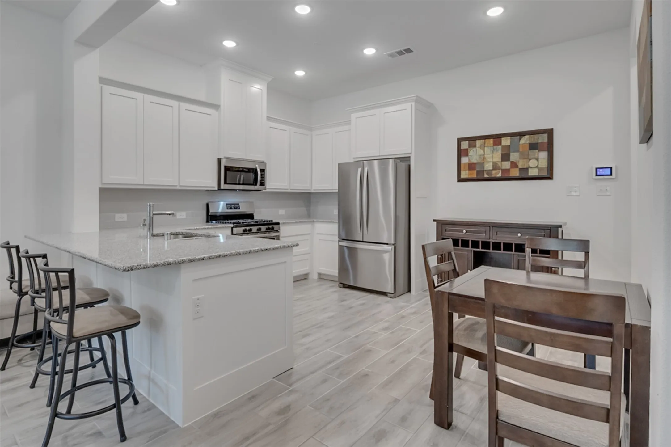 Kitchen featuring white cabinetry, stainless steel appliances, granite countertops, a built-in kitchen island with a sink, and wood-finish flooring