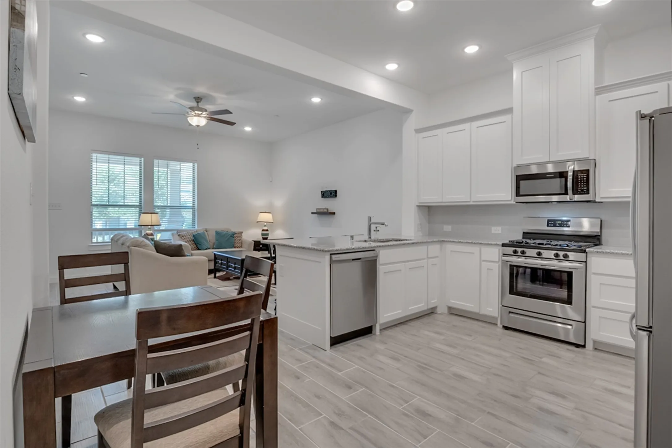 Kitchen with white cabinetry, stainless steel appliances, light-toned countertops, and wood-finish flooring