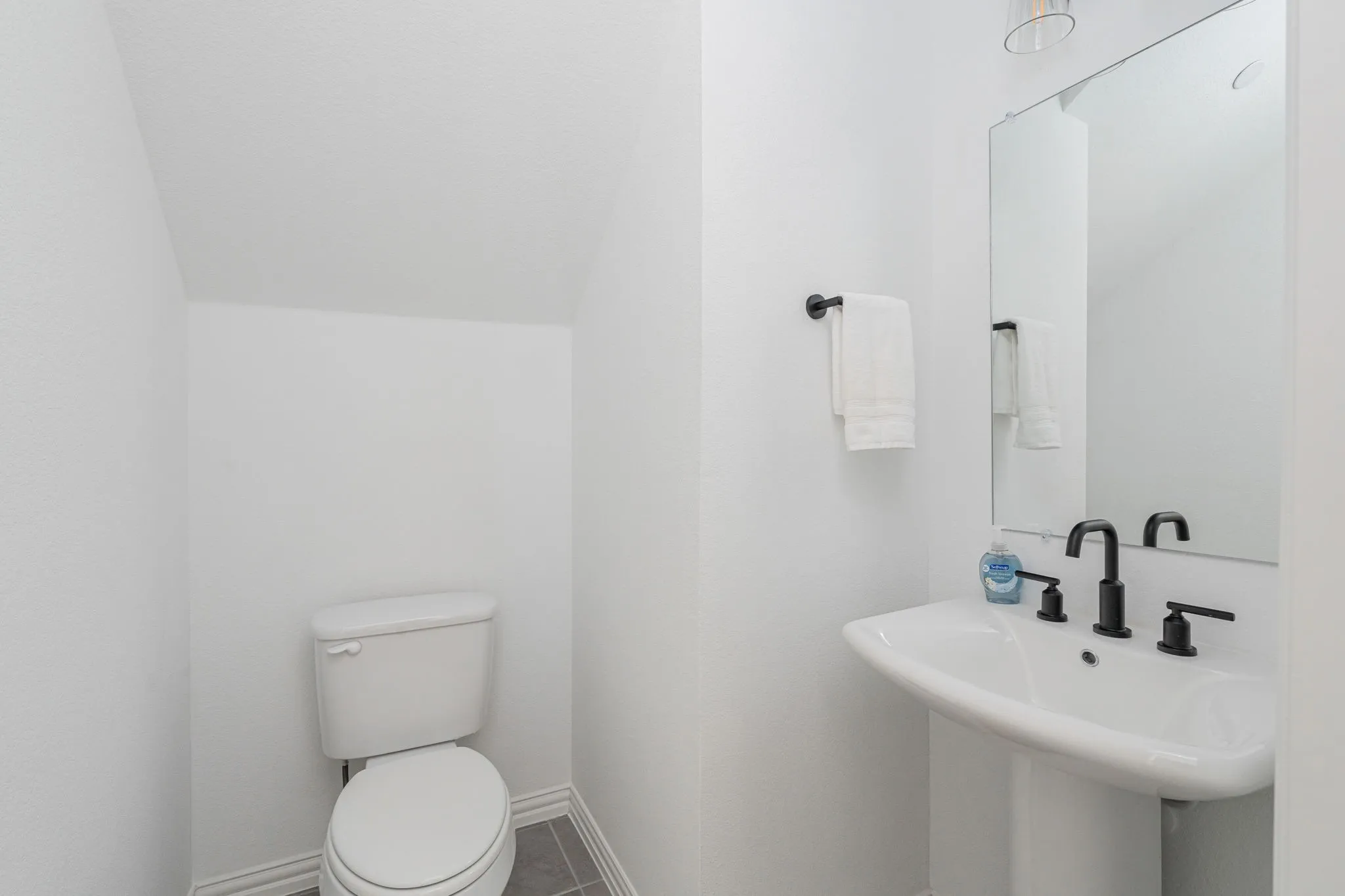 Charming 1st floor powder bath offers a clean, contemporary aesthetic with a pedestal sink, modern matte-black fixtures, coordinating hardware, and oversized mirror.