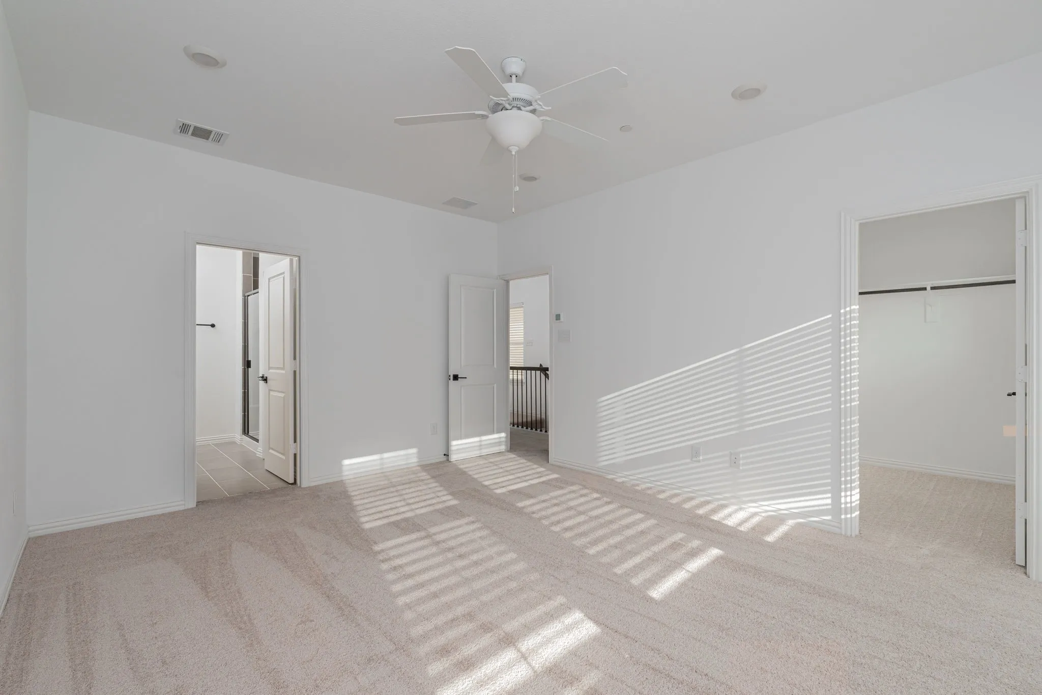 This spacious primary bedroom offers a bright, tranquil retreat with plush carpeting, ceiling fan, abundant natural light, and convenient access to the en-suite bath and walk-in closet.