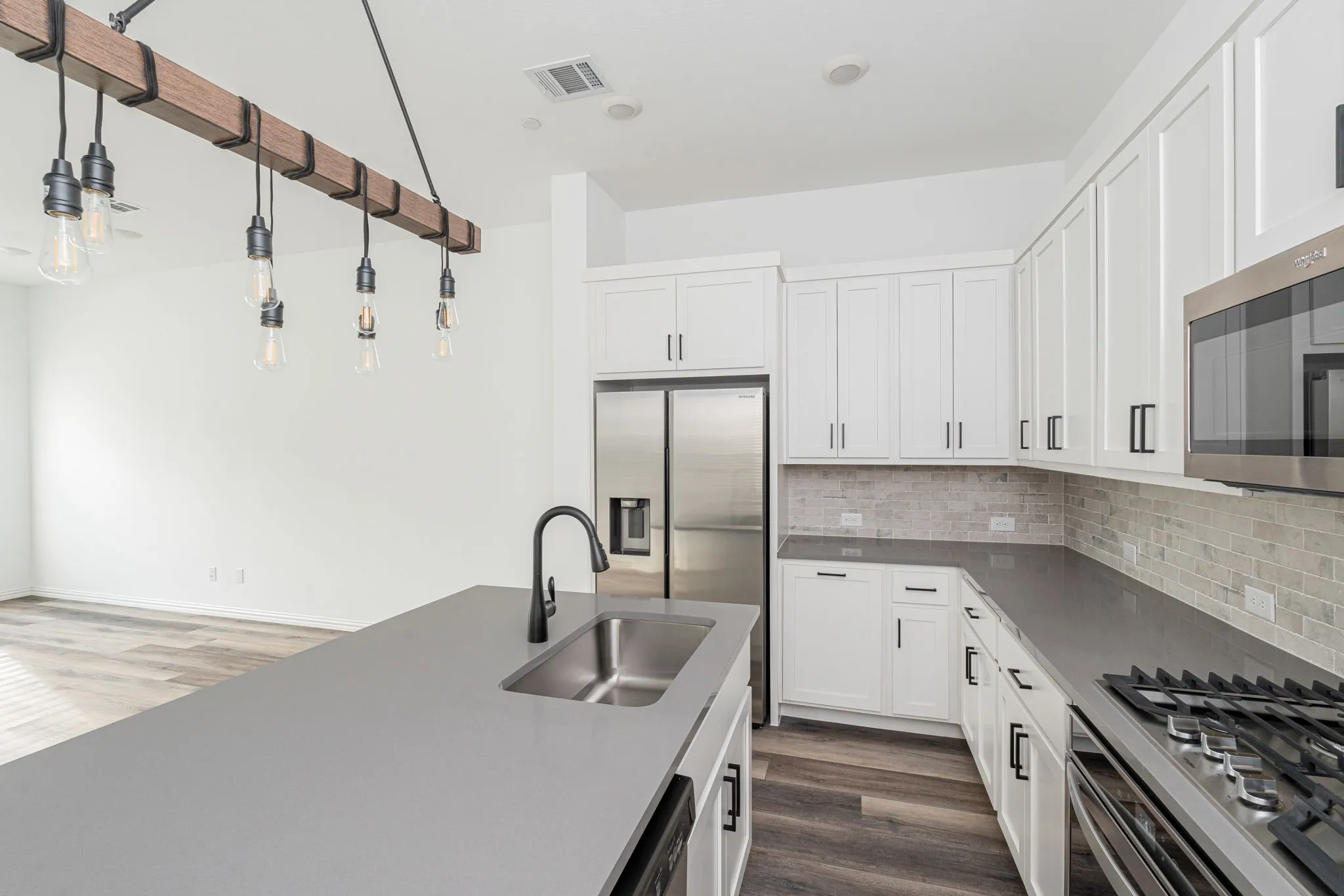 A closer look at the thoughtfully designed kitchen reveals generous workspace, plentiful cabinetry, modern stainless-steel appliances, a large island, and a stylish pendant light fixture overlooking the open living area.