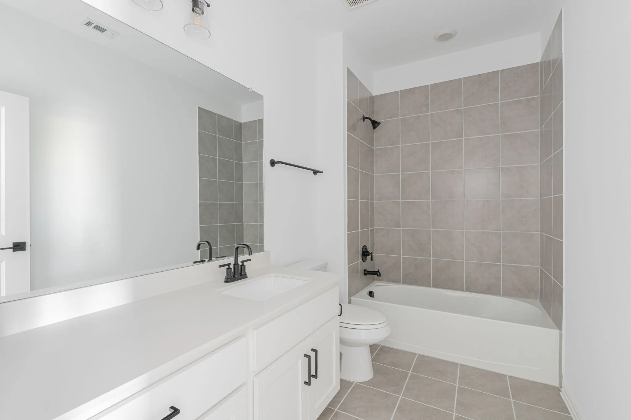 Relaxing secondary bath showcases a large soaking tub/shower combo with a tile surround, modern matte-black fixtures, and an expansive vanity designed for everyday comfort and convenience.