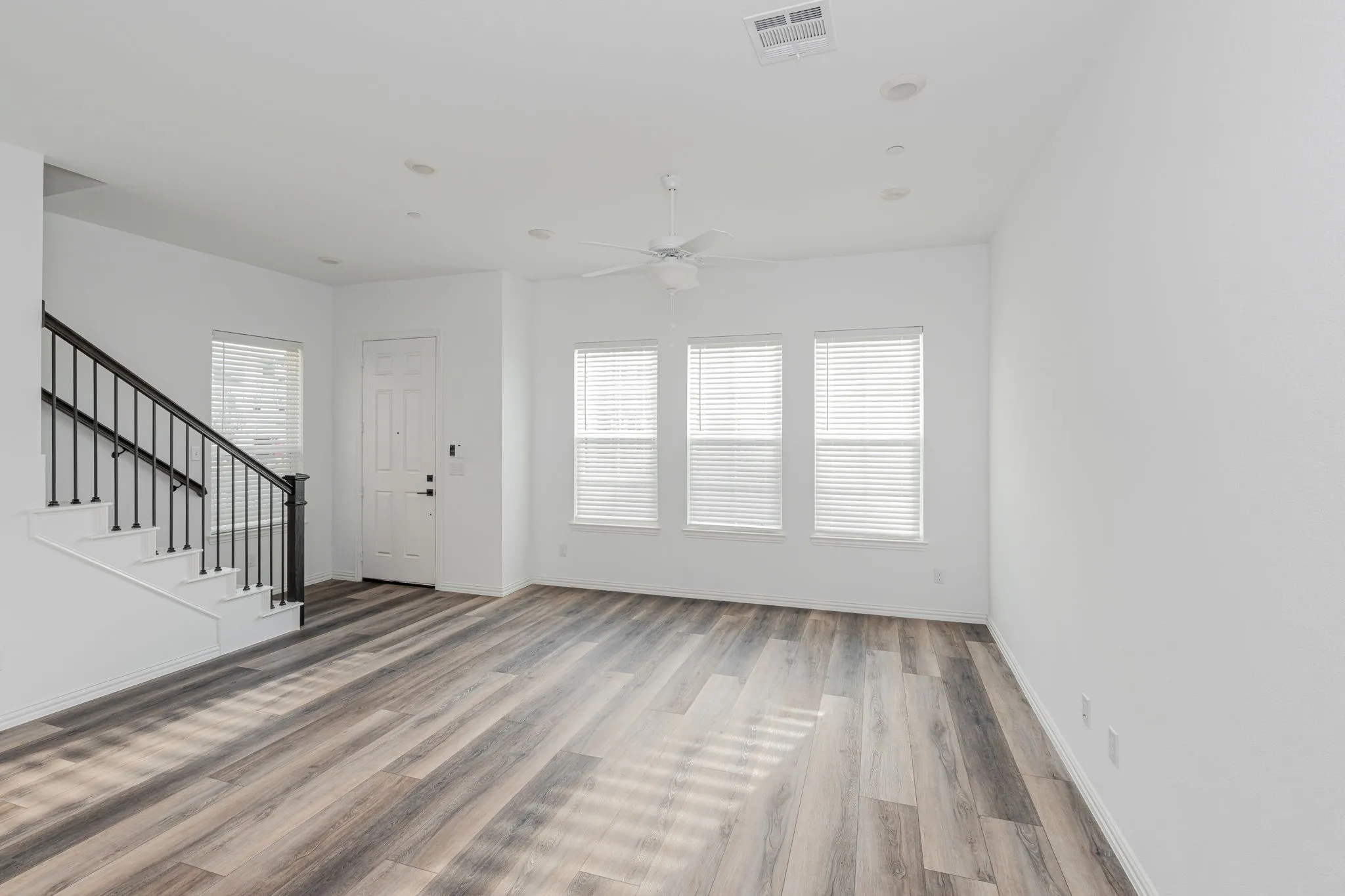 Expansive main living space showcases wide-plank flooring, abundant natural light, and an open layout flowing effortlessly toward the kitchen and staircase leading to the 2nd floor.