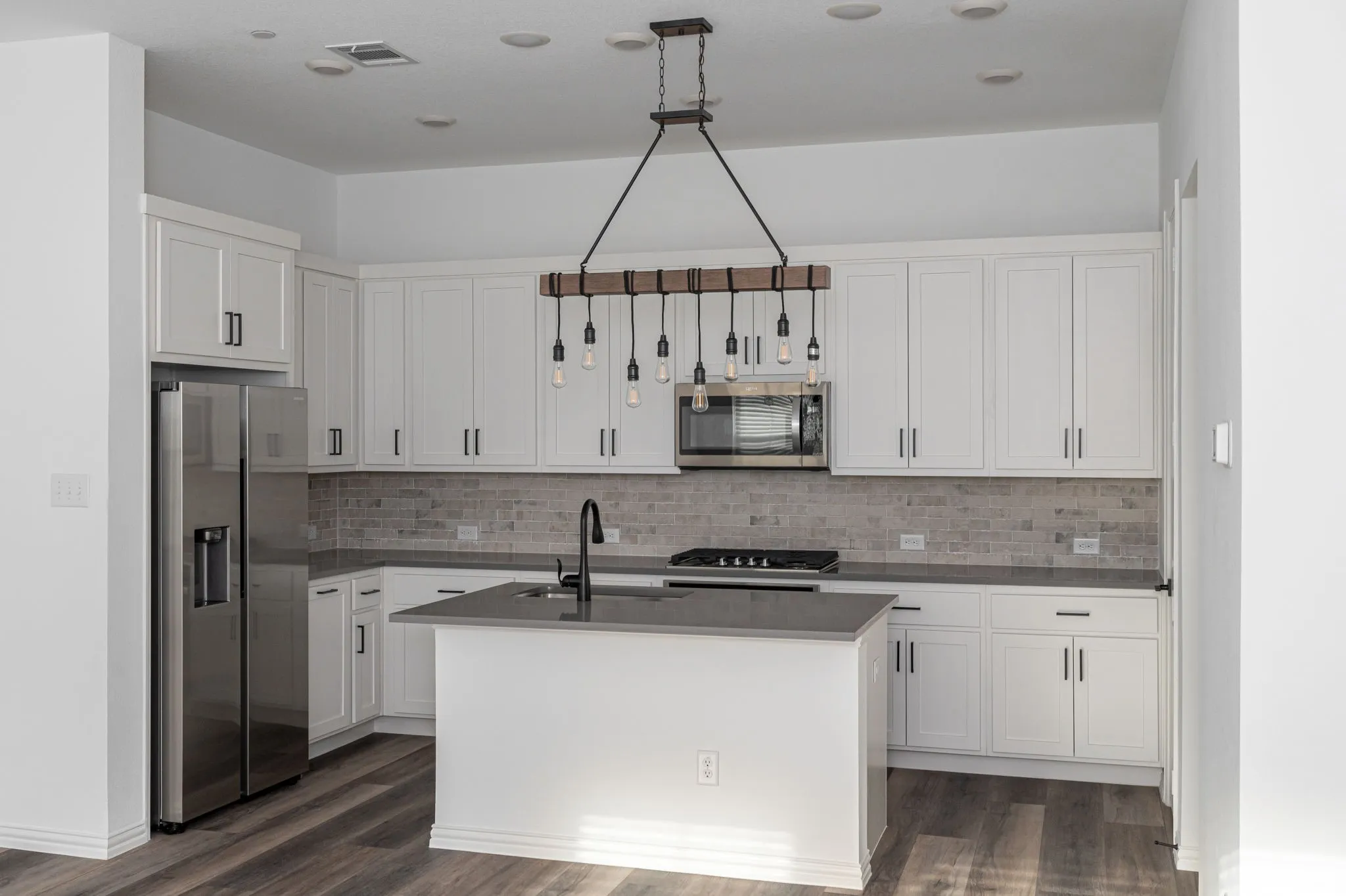 Bright, beautifully appointed kitchen featuring an abundance of crisp white cabinetry, sleek quartz countertops, subway tile backsplash, stainless-steel appliances, gas cooking, and a generously sized center island with undermount sink.