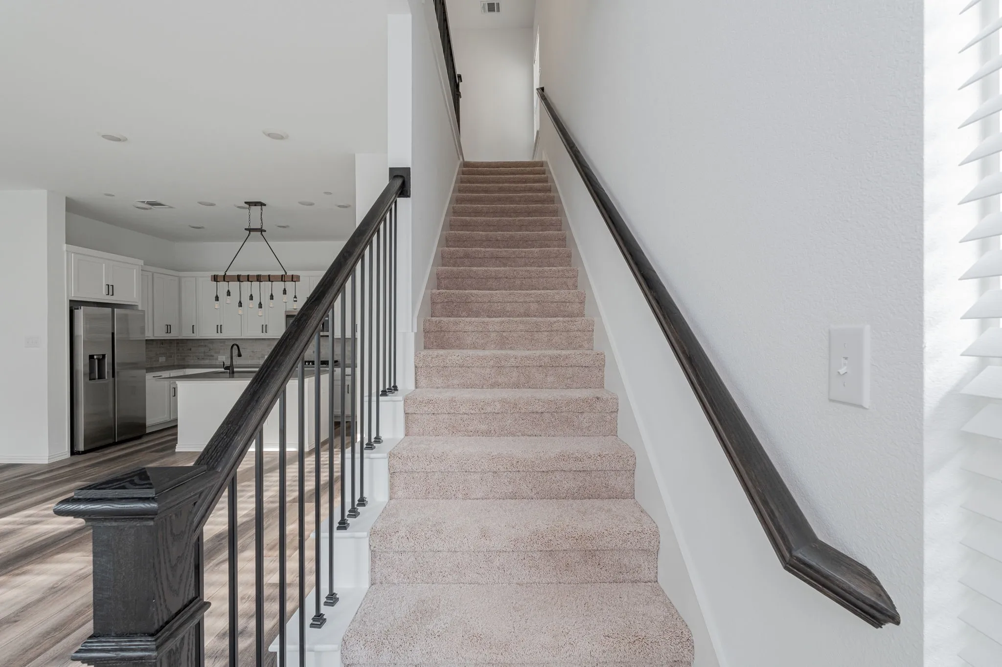Elegant staircase features warm wood handrails, decorative black iron balusters, and plush carpeting, creating a striking architectural focal point connecting the home's two levels.