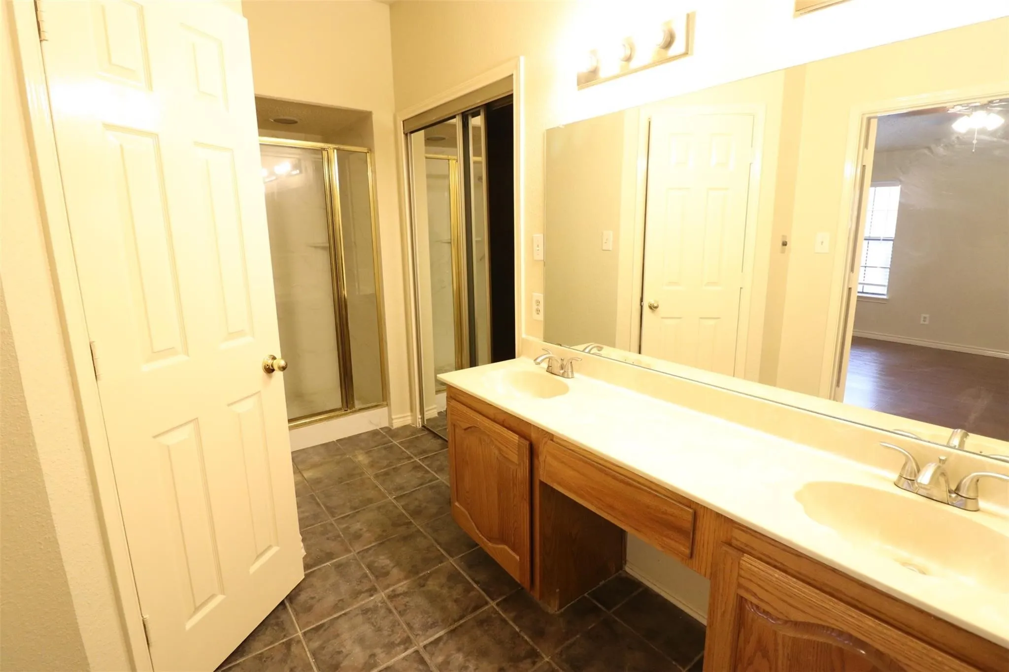 Dual vanity with integrated sinks, wood-finish cabinetry, full-width mirror, and a shower with a sliding glass enclosure