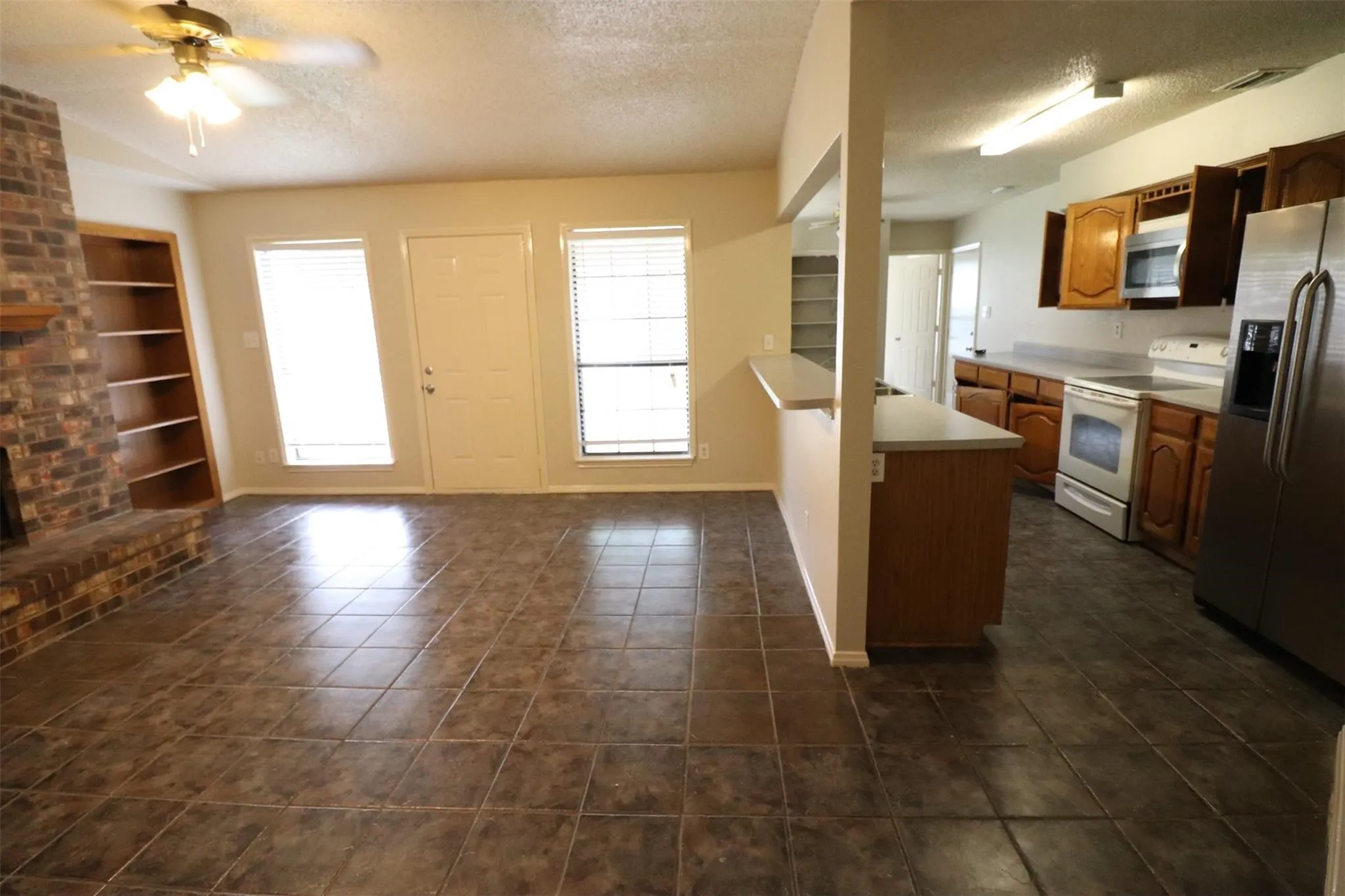 Brick fireplace with built-in shelving, tile flooring, and a ceiling fan