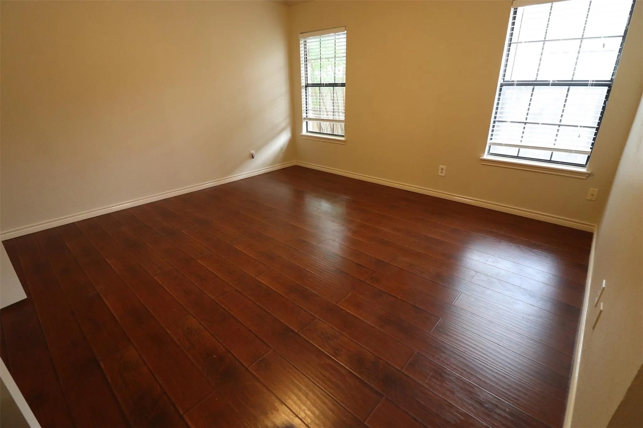 Rich wood-finish flooring, two large windows with blinds, and neutral wall tones