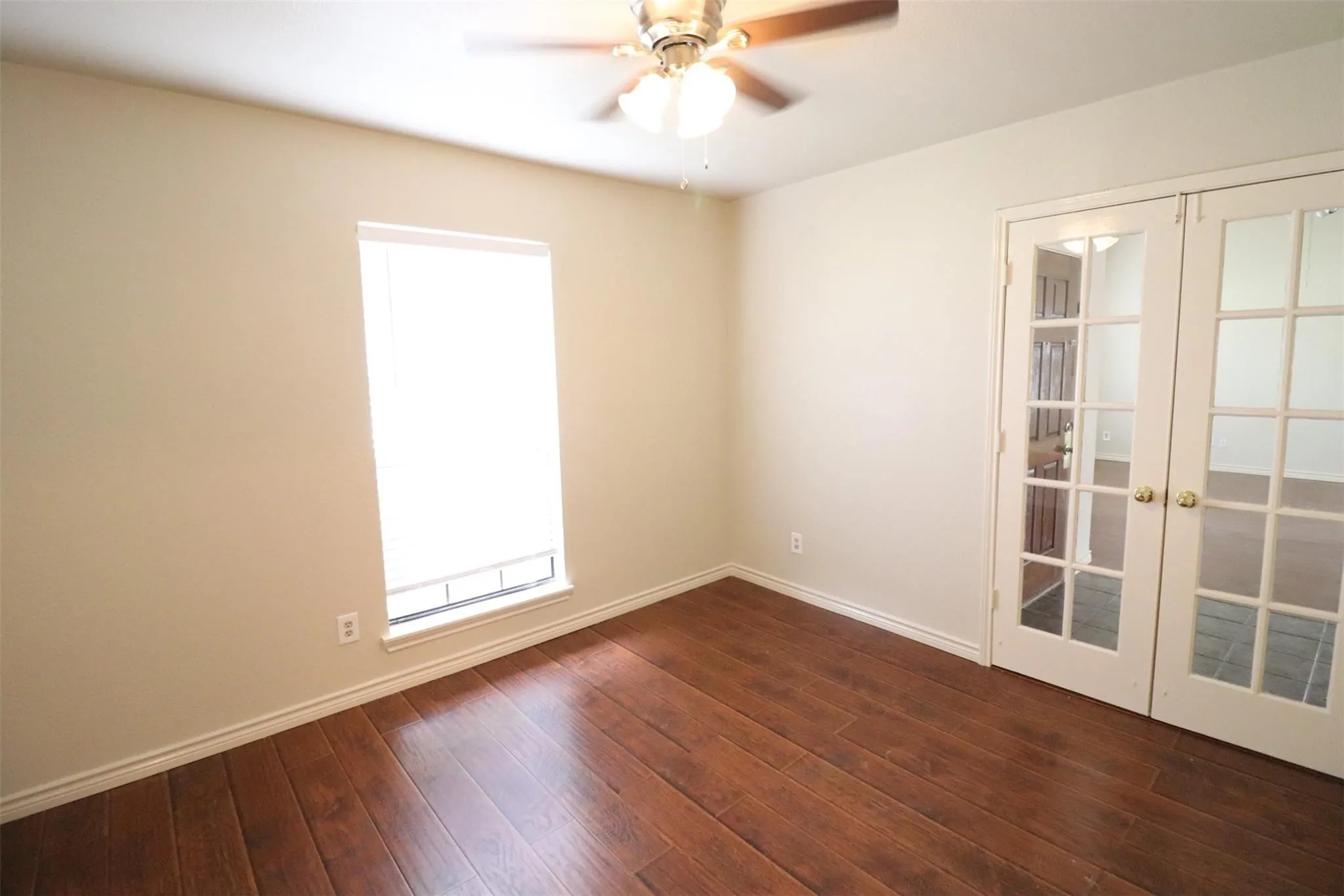 Wood-finish flooring, neutral wall tones, window with roller shade, and double French doors with clear glass panes
