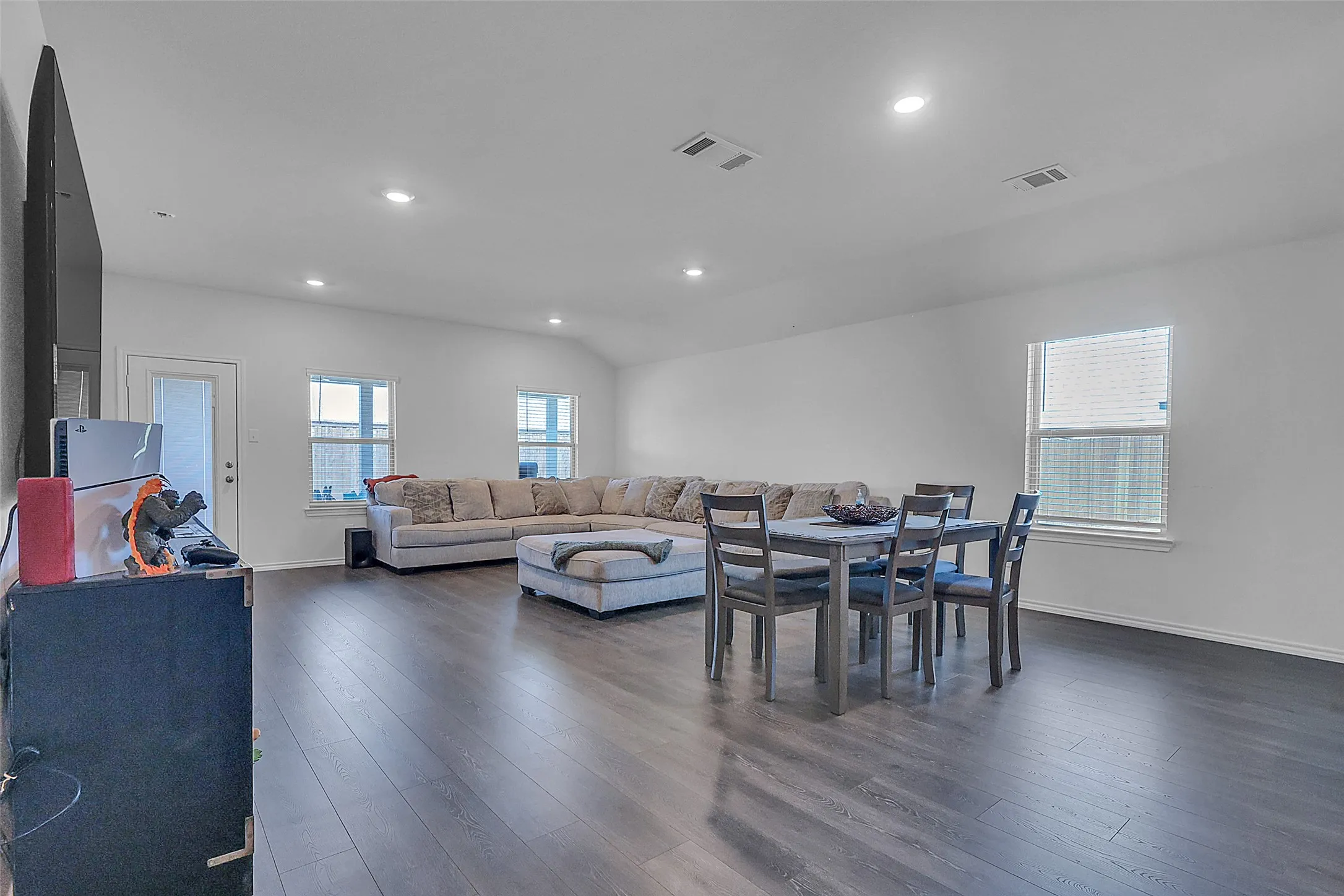 Spacious open-concept room featuring dark wood-finish flooring, recessed lighting, and multiple windows