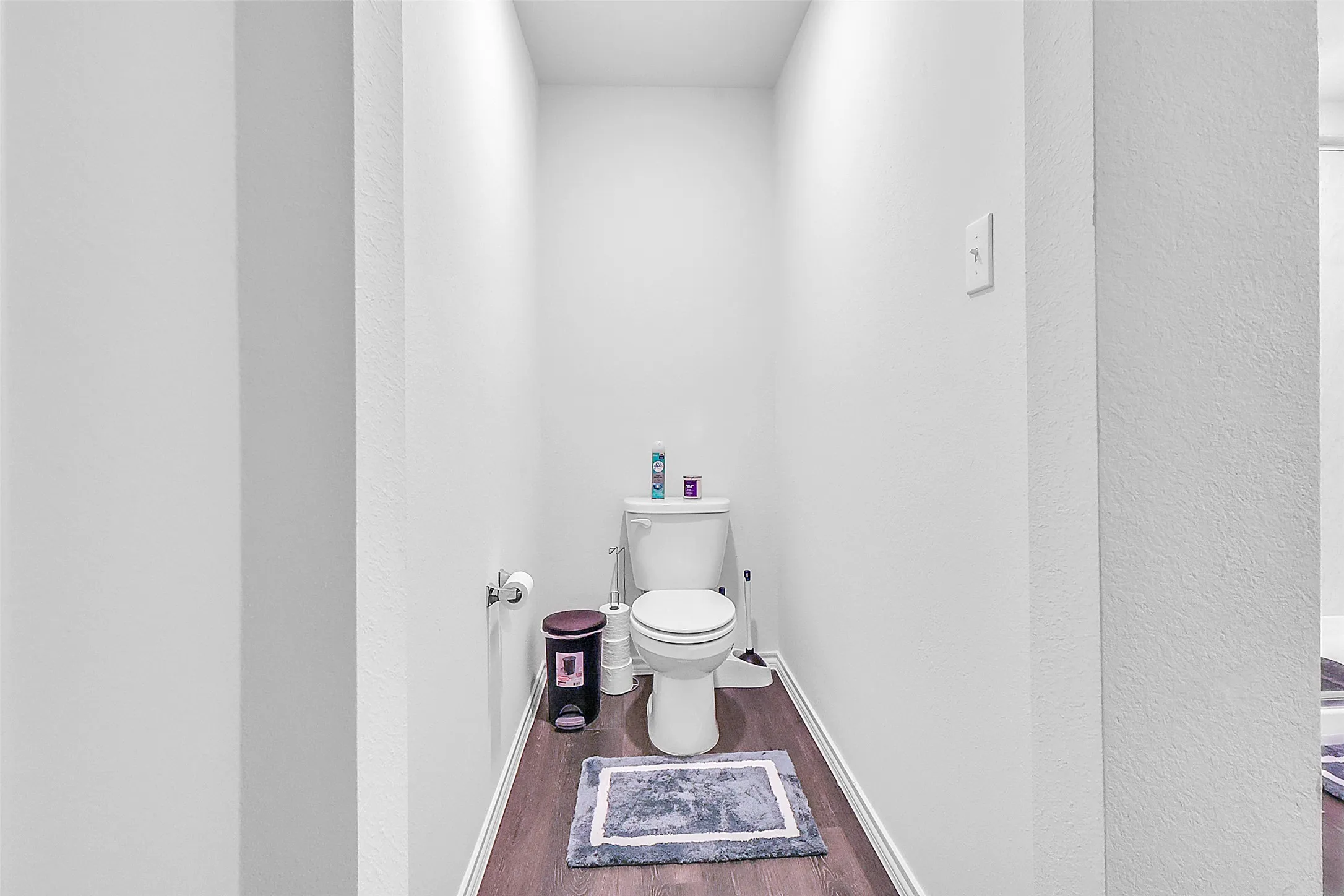 White toilet with a toilet paper holder and wood-finish flooring