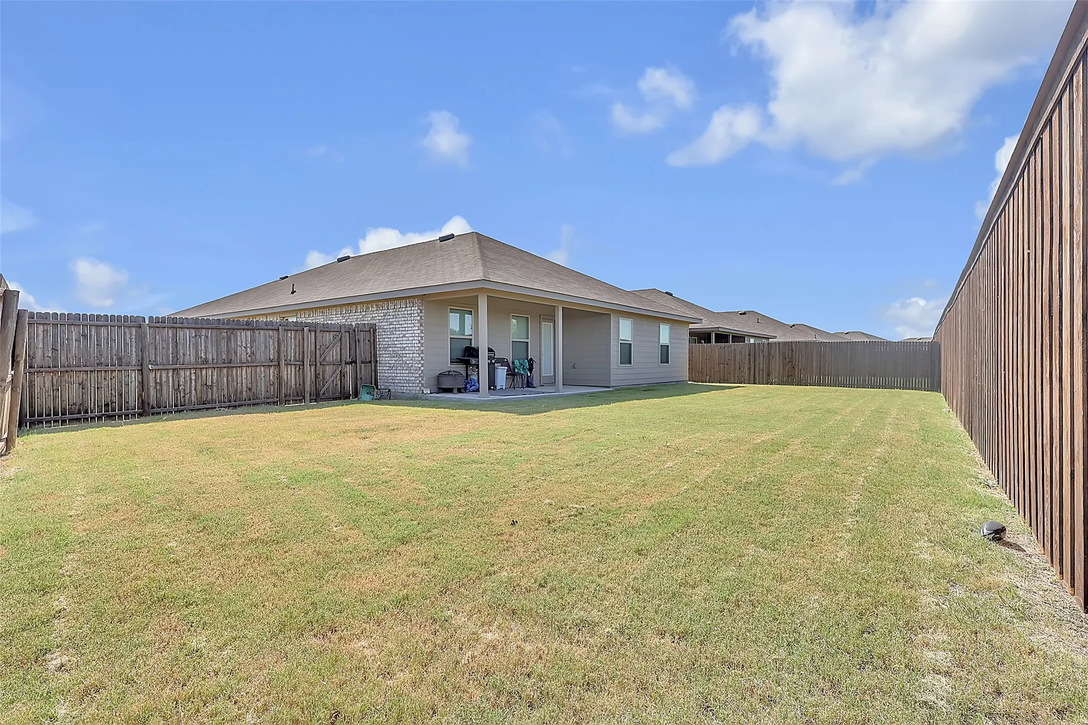 Expansive backyard with a covered patio, full privacy fencing, brick exterior, and multiple​​‌​​​​‌​​‌‌​‌‌​​​‌‌​‌​‌​‌​​​‌​​ windows