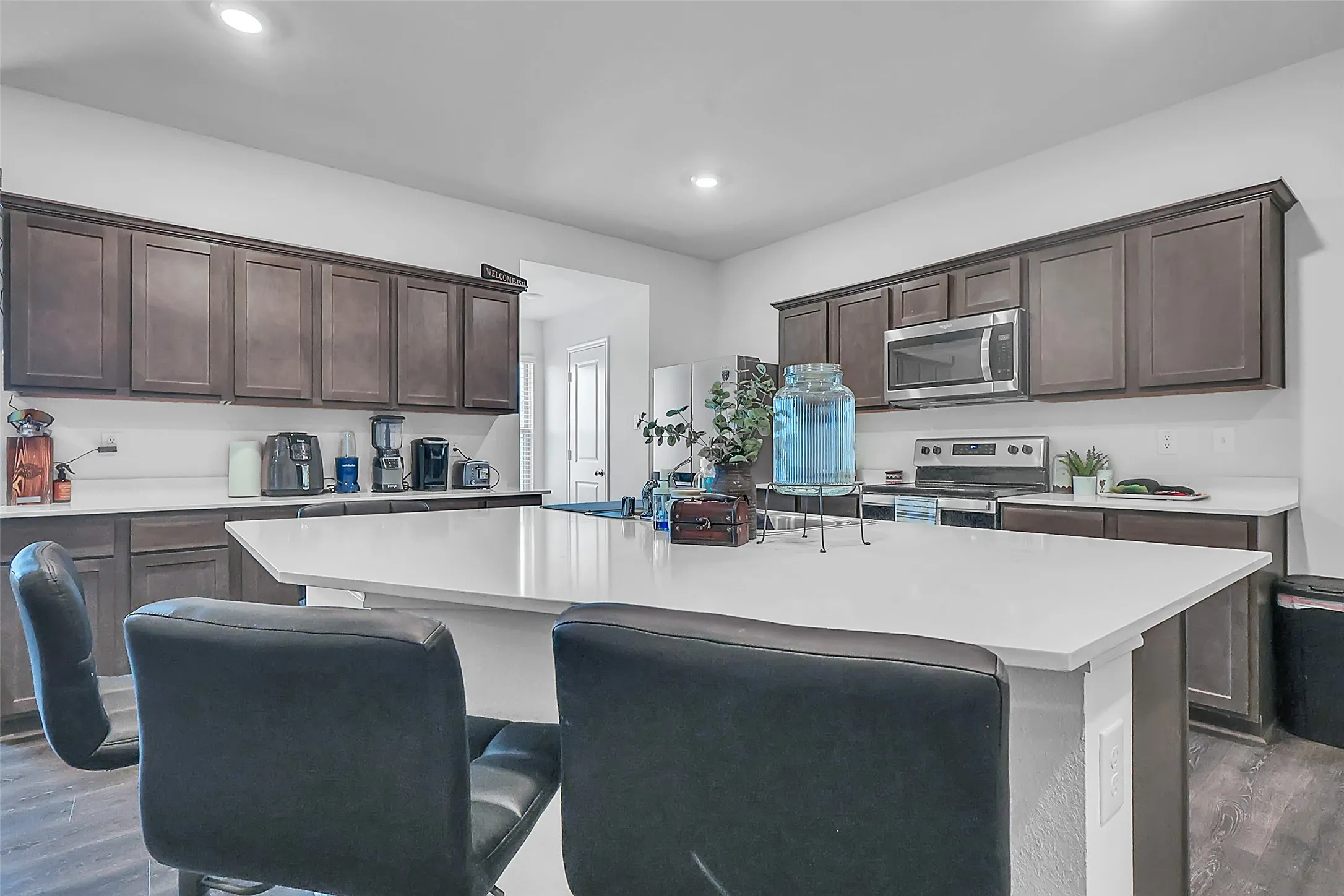 Central kitchen island with white countertop, dark wood-finish cabinetry, stainless steel microwave, and stainless steel range