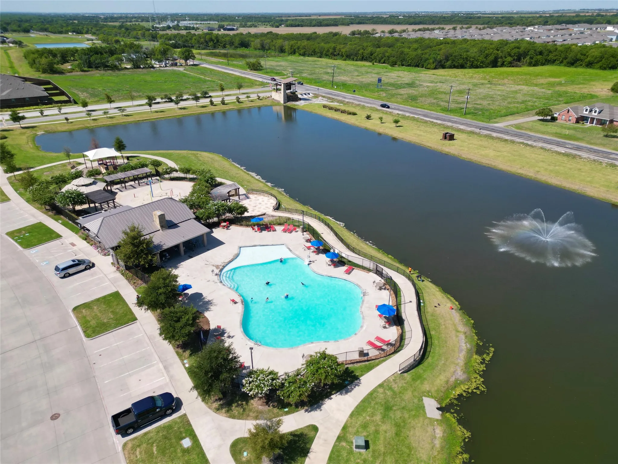 Community pool with integrated lounge areas, adjacent covered pavilion, and surrounding manicured green space
