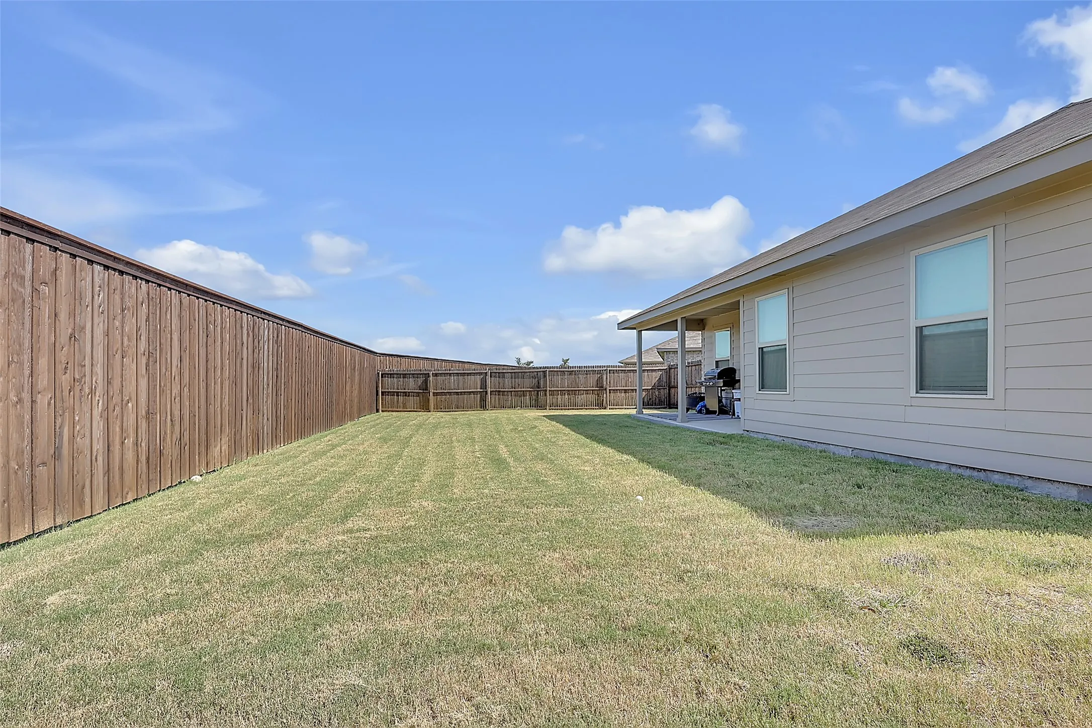 Expansive backyard featuring a manicured lawn, full privacy fencing, and a covered patio