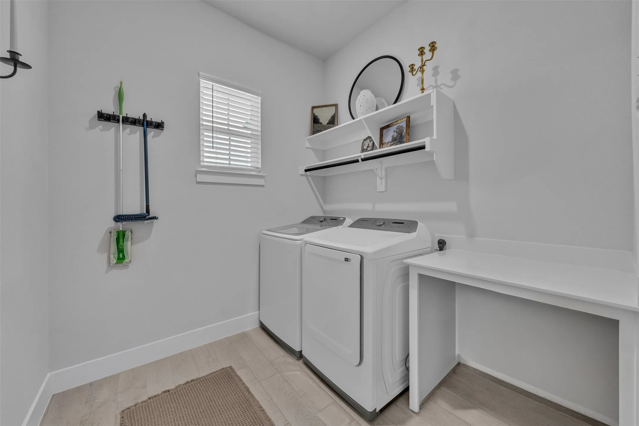 Laundry area featuring light-toned flooring, a window with blinds, and white built-in shelving