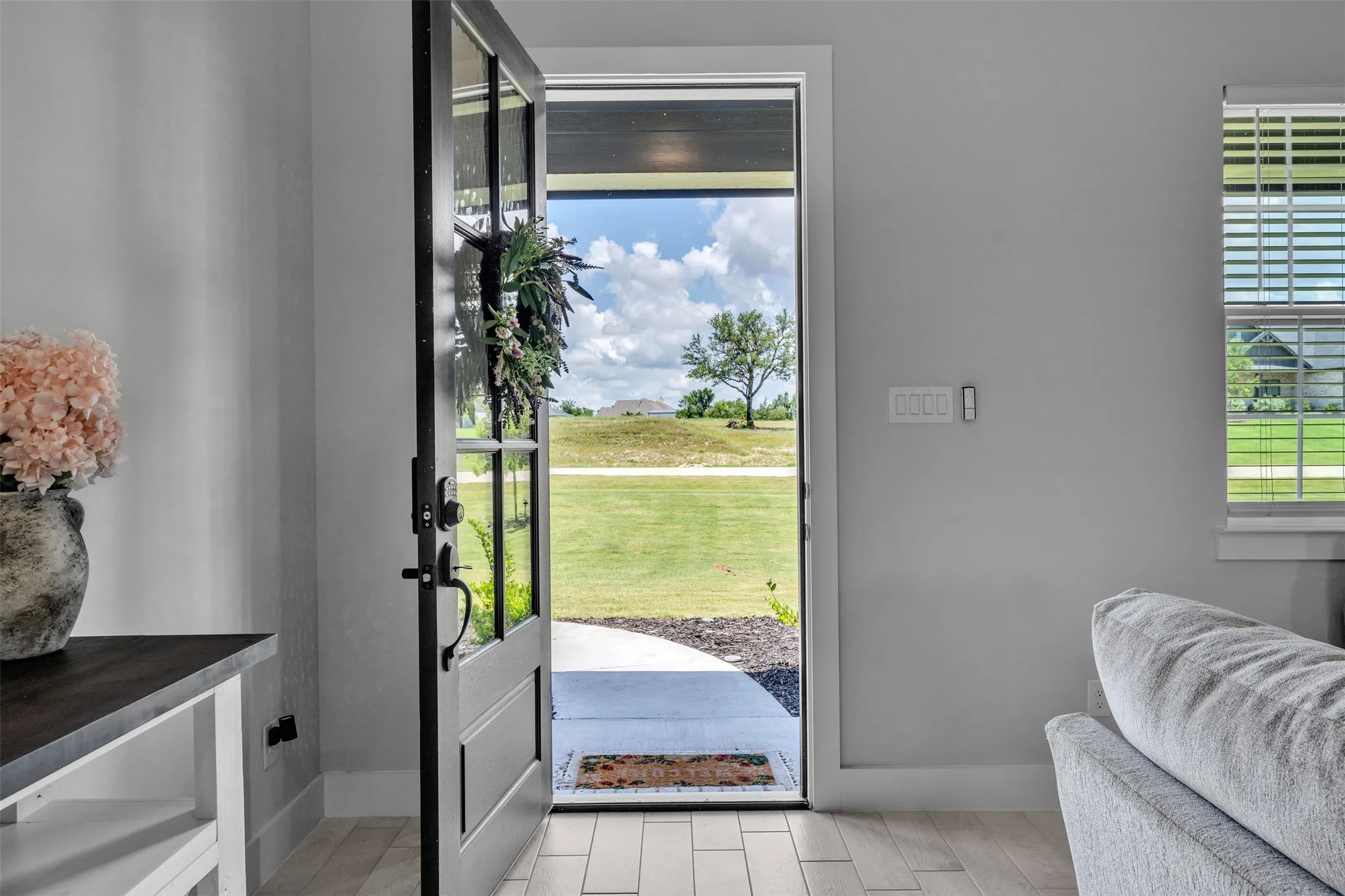Entryway featuring a partially open door with glass panels, light wood-finish flooring, and a side window with blinds
