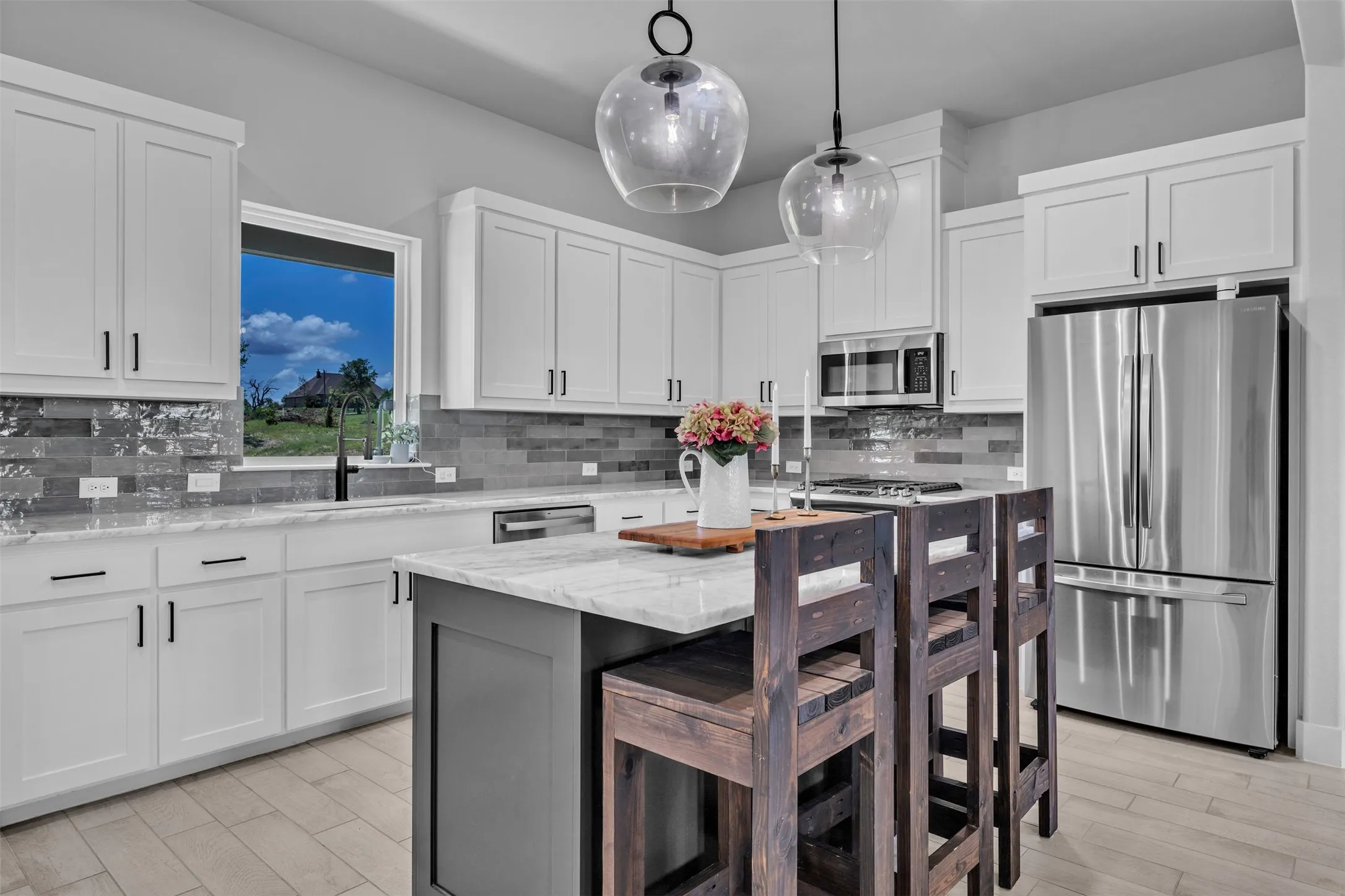 Kitchen featuring white shaker cabinetry, stainless steel appliances, a center island with bar seating, and light-toned wood-finish flooring