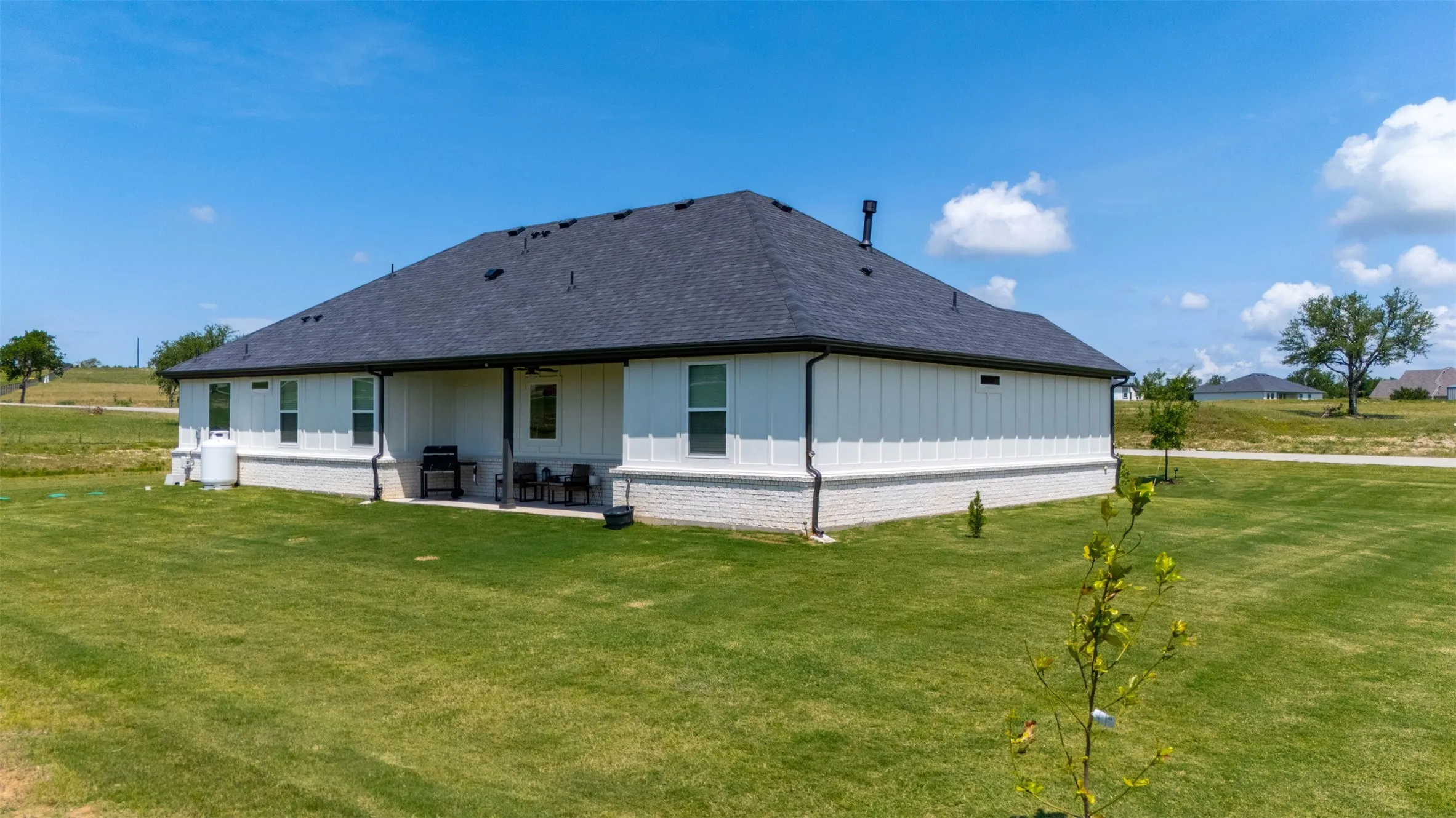 Back exterior featuring a covered patio, dark asphalt shingle roof, and white board-and-batten siding