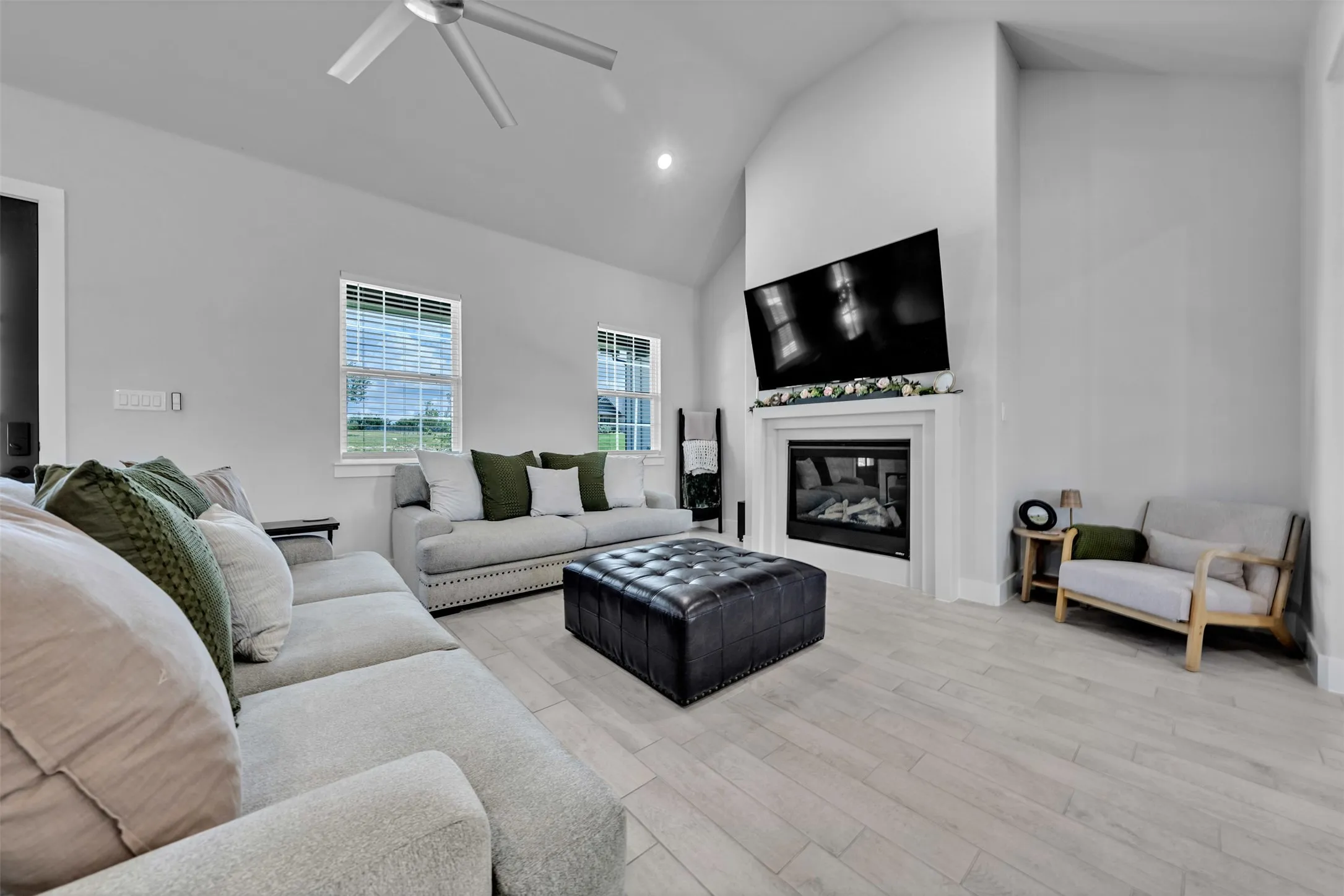 Vaulted ceiling with a contemporary ceiling fan, light wood-finish flooring, white fireplace with a mantel, and recessed lighting