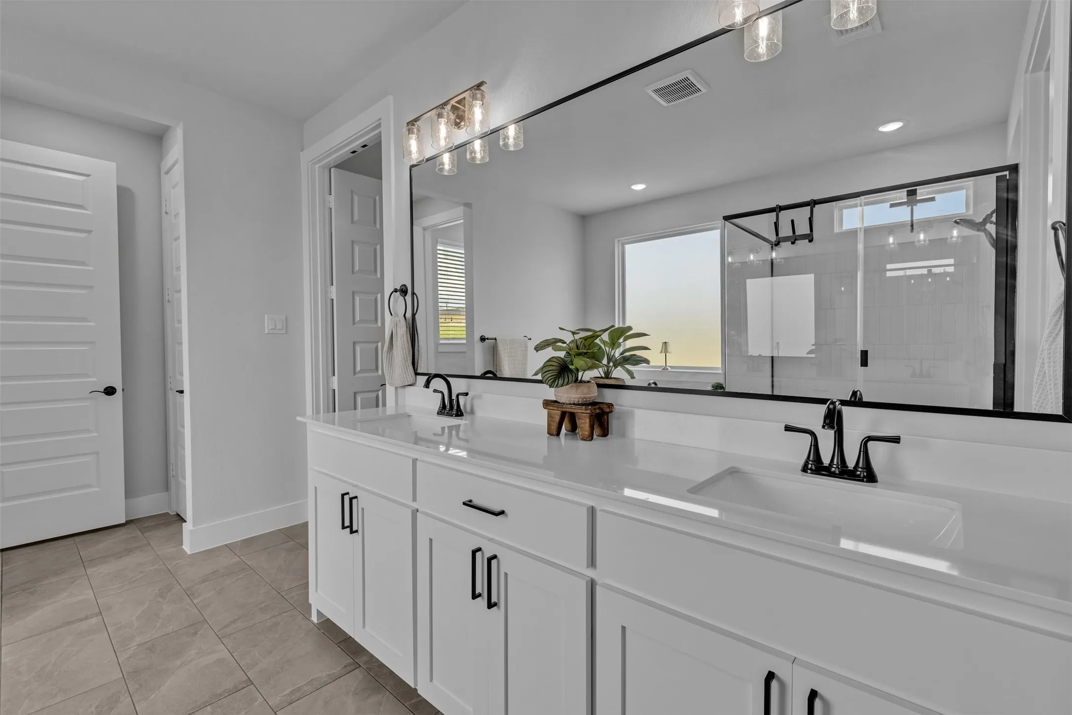 Double vanity with undermount sinks, white cabinetry, matte black hardware, and an expansive wall-mounted mirror