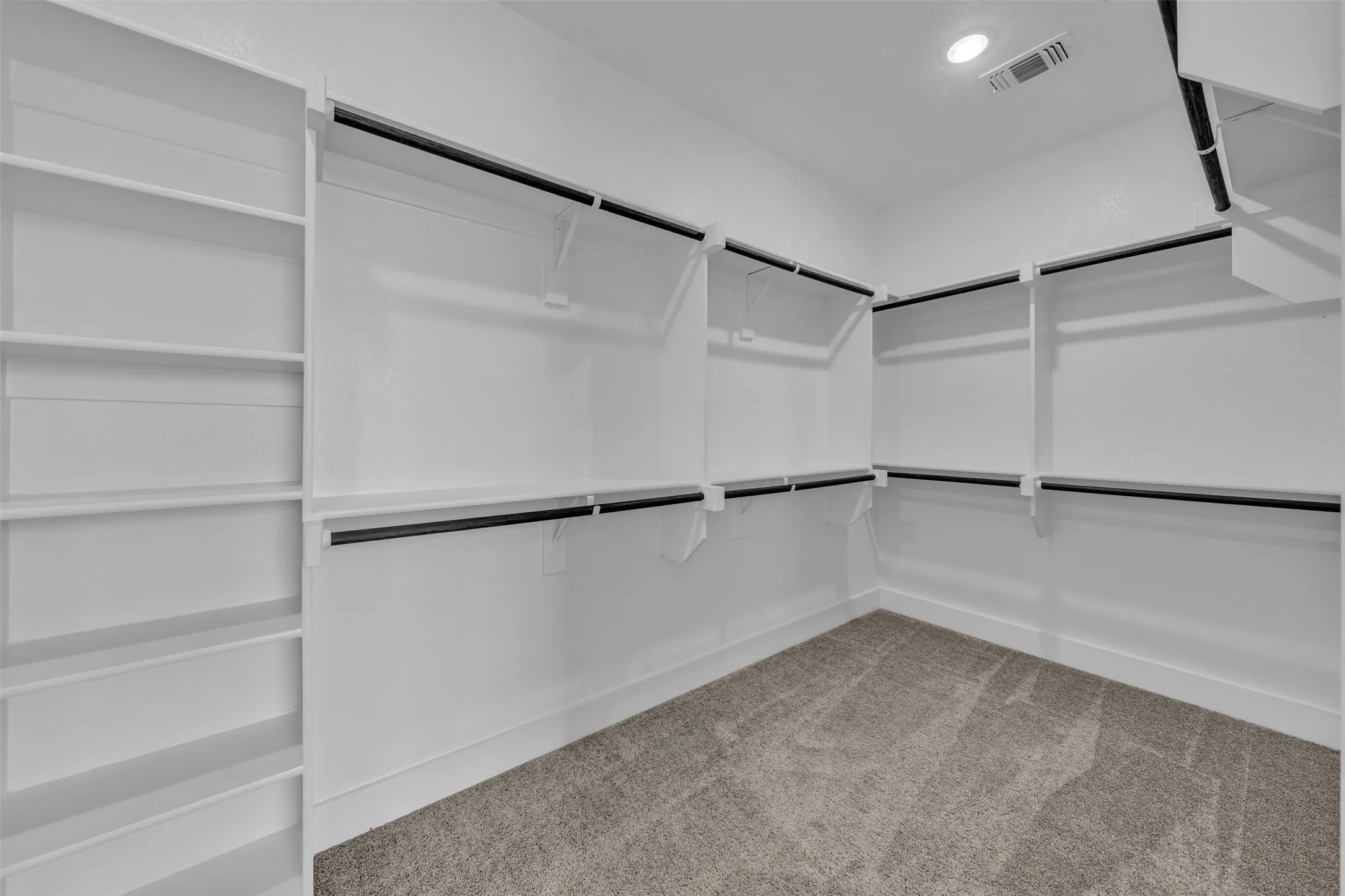 Walk-in closet with built-in shelving, multiple hanging rods, white walls, and carpet flooring
