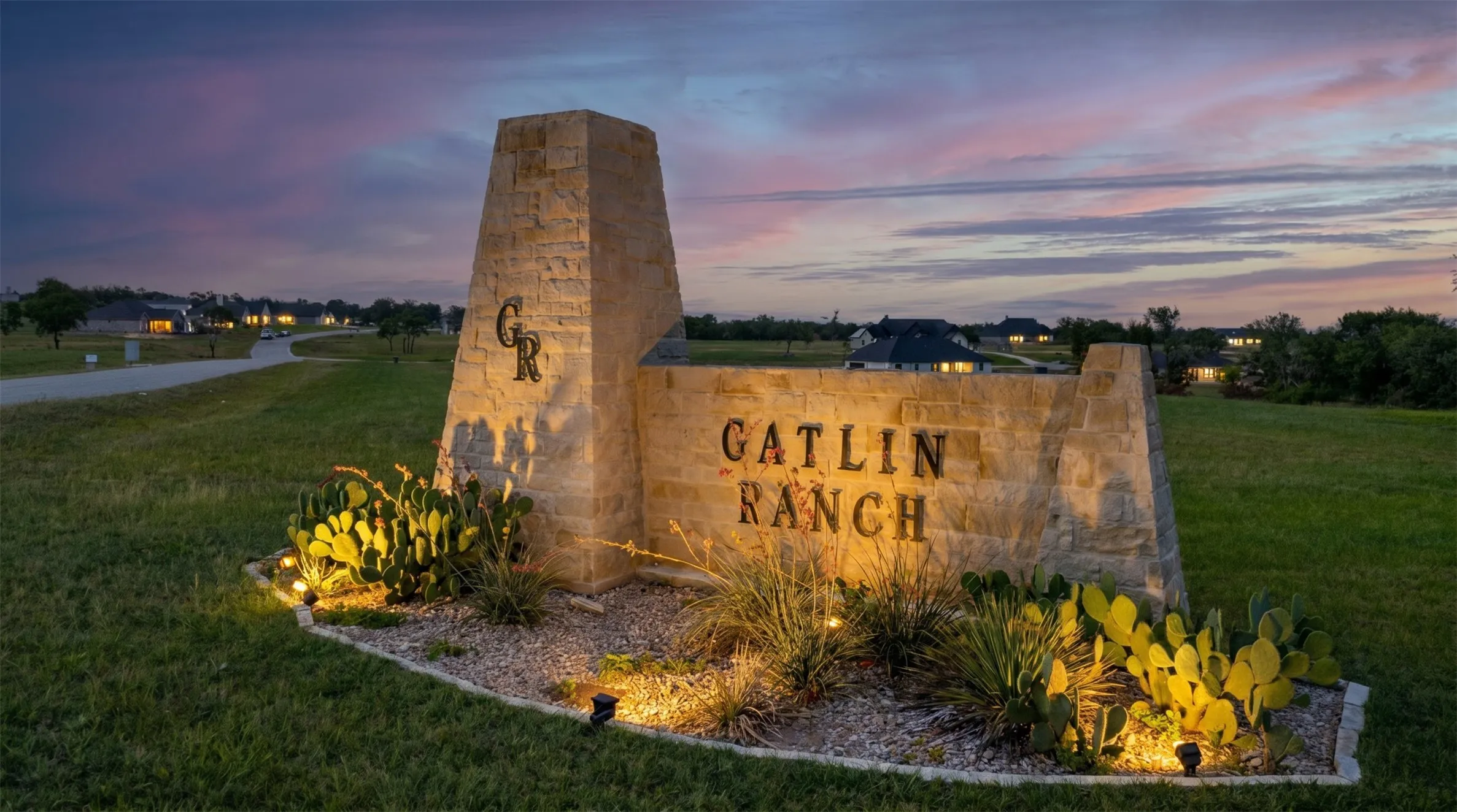Stone entrance monument with integrated lighting, gravel landscaping, and desert plantings
