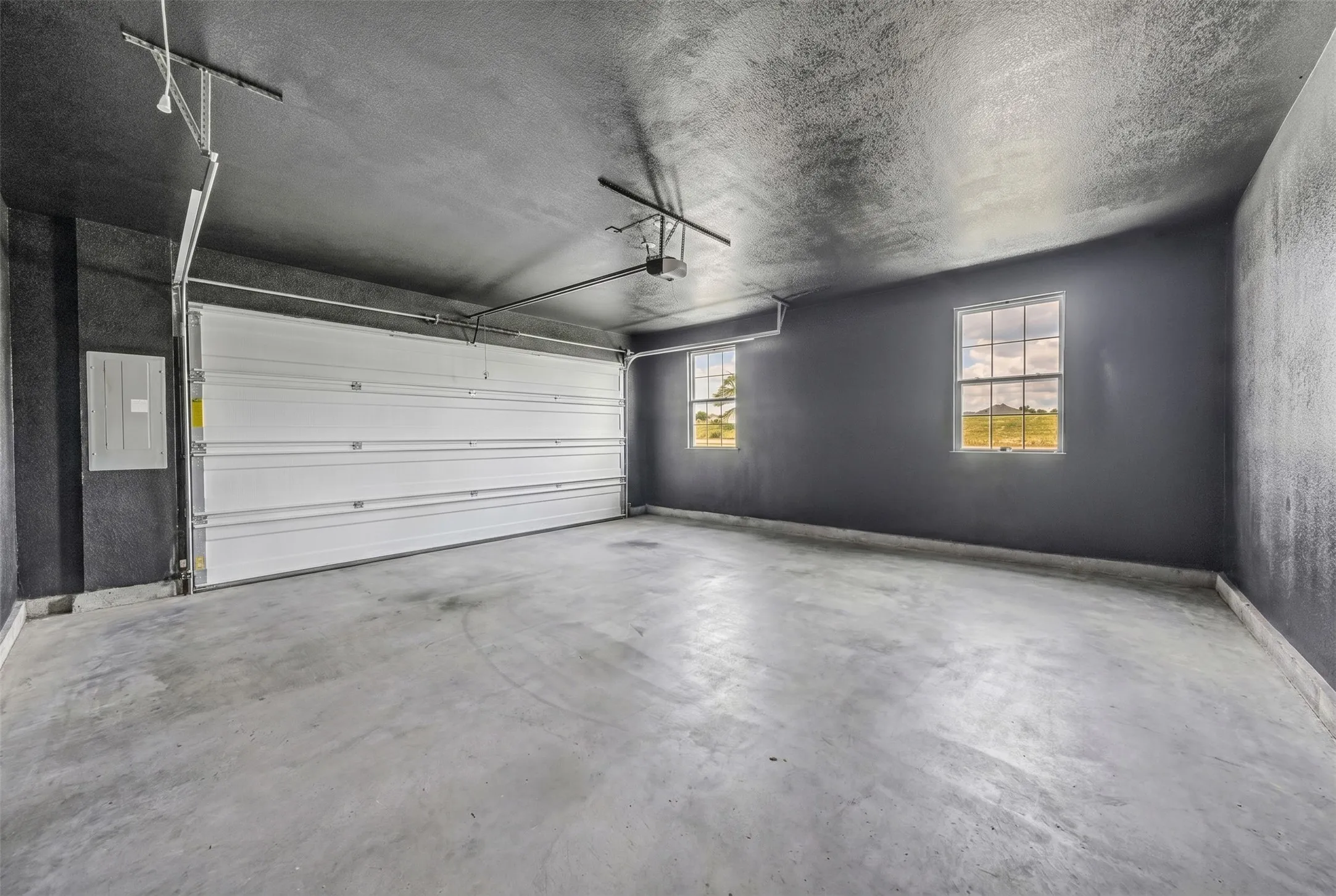 Attached garage with a white sectional door, concrete flooring, and two double-hung windows