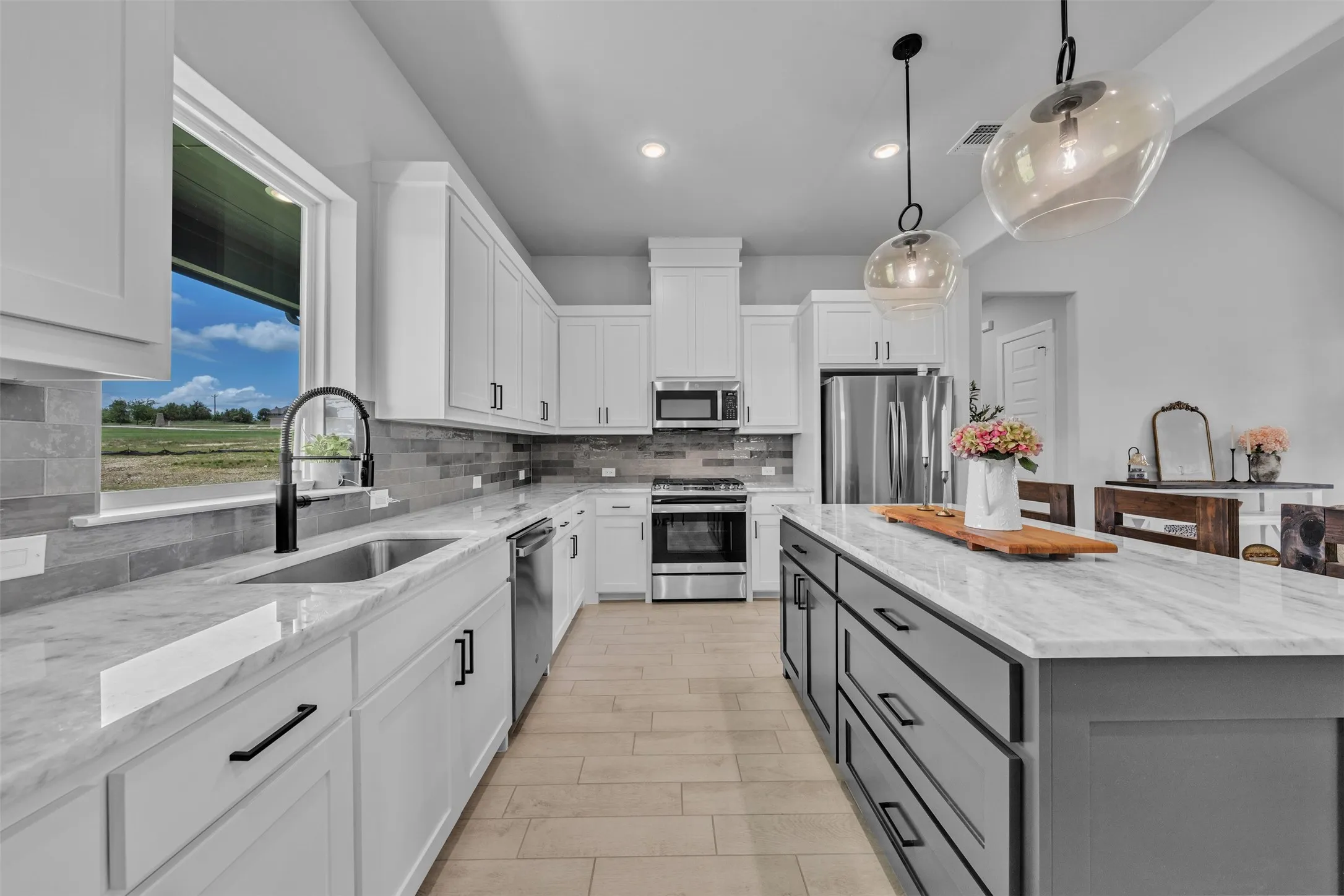 Kitchen featuring a large window, white cabinetry, a center island with a light-toned countertop, stainless steel appliances, and wood-finish flooring