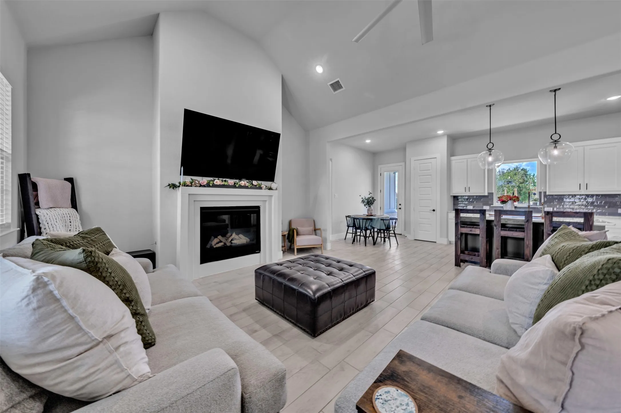 Vaulted ceilings, a built-in fireplace, recessed lighting, wood-finish flooring, and a kitchen island with pendant lighting