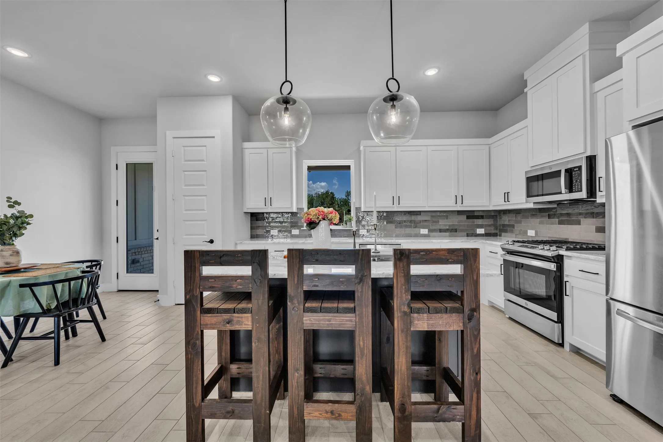 Contemporary kitchen featuring stainless steel appliances, white cabinetry, a tiled backsplash, and light wood-finish flooring
