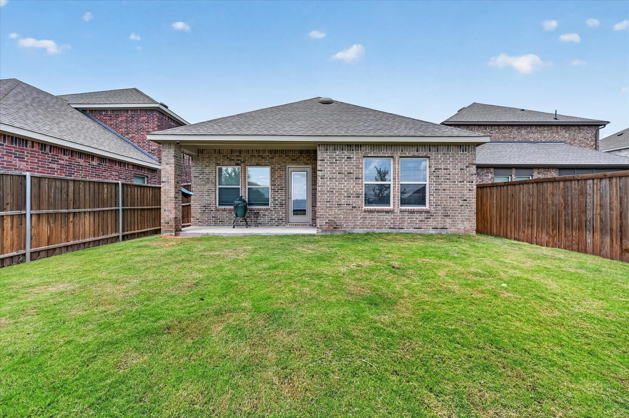Expansive backyard featuring a covered patio, brick exterior, and a privacy fence