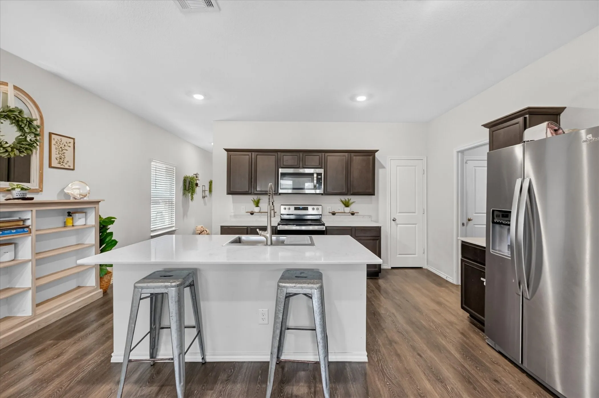 Kitchen with a large island featuring a sink, dark wood-finish cabinetry, stainless steel appliances, and light-colored countertops