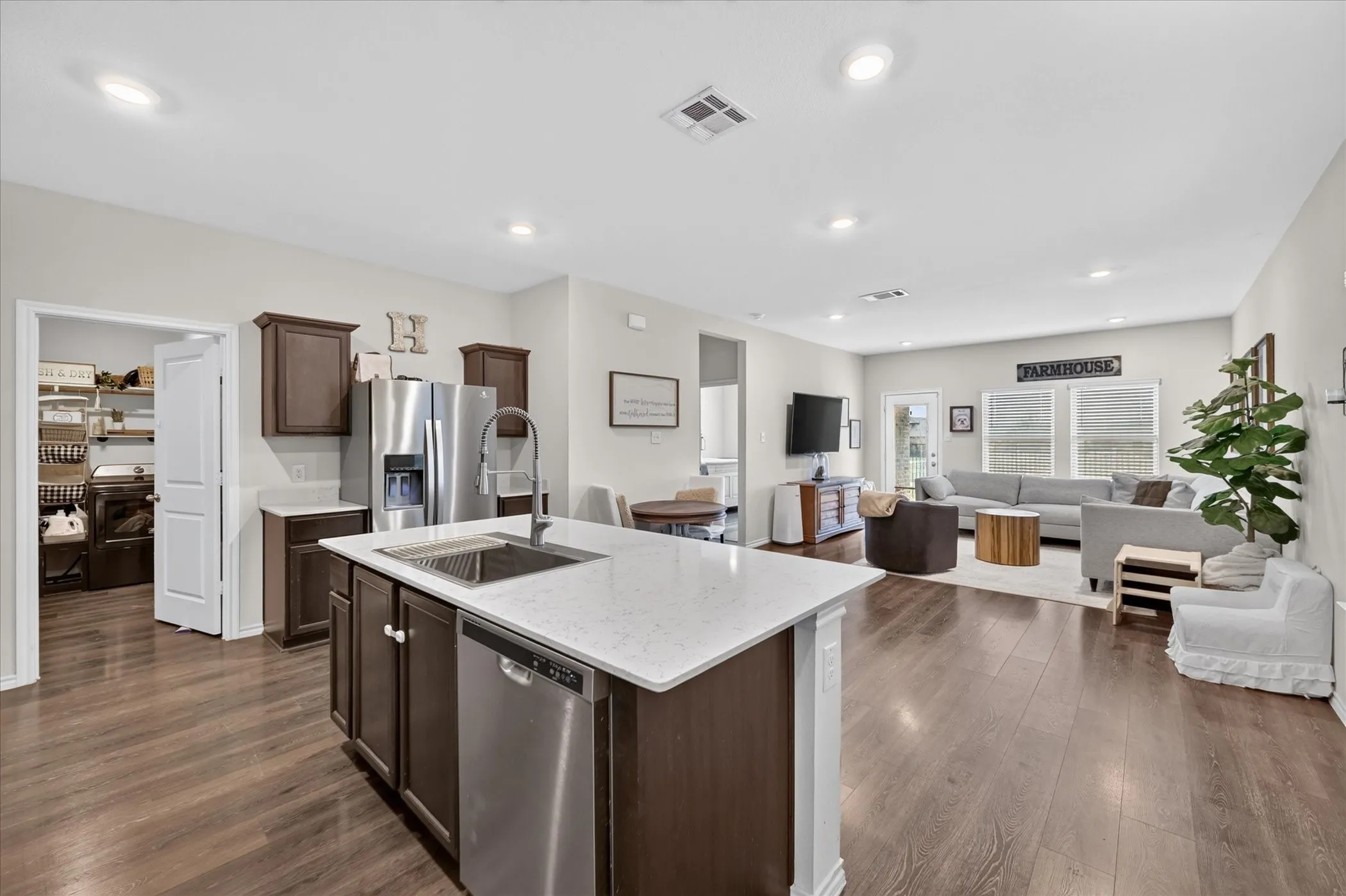 Open-concept living space featuring wood-finish flooring, recessed lighting, and a kitchen island with an undermount sink and stone countertop