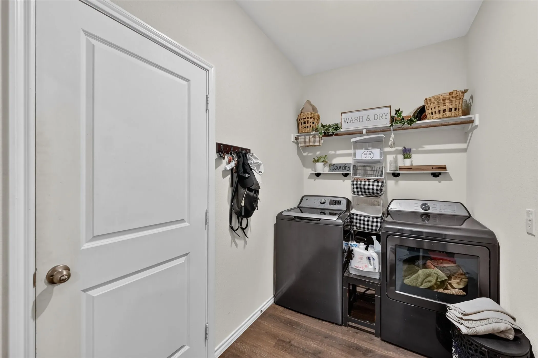 Laundry area with wood-finish flooring, two wall-mounted shelves, and a white paneled door
