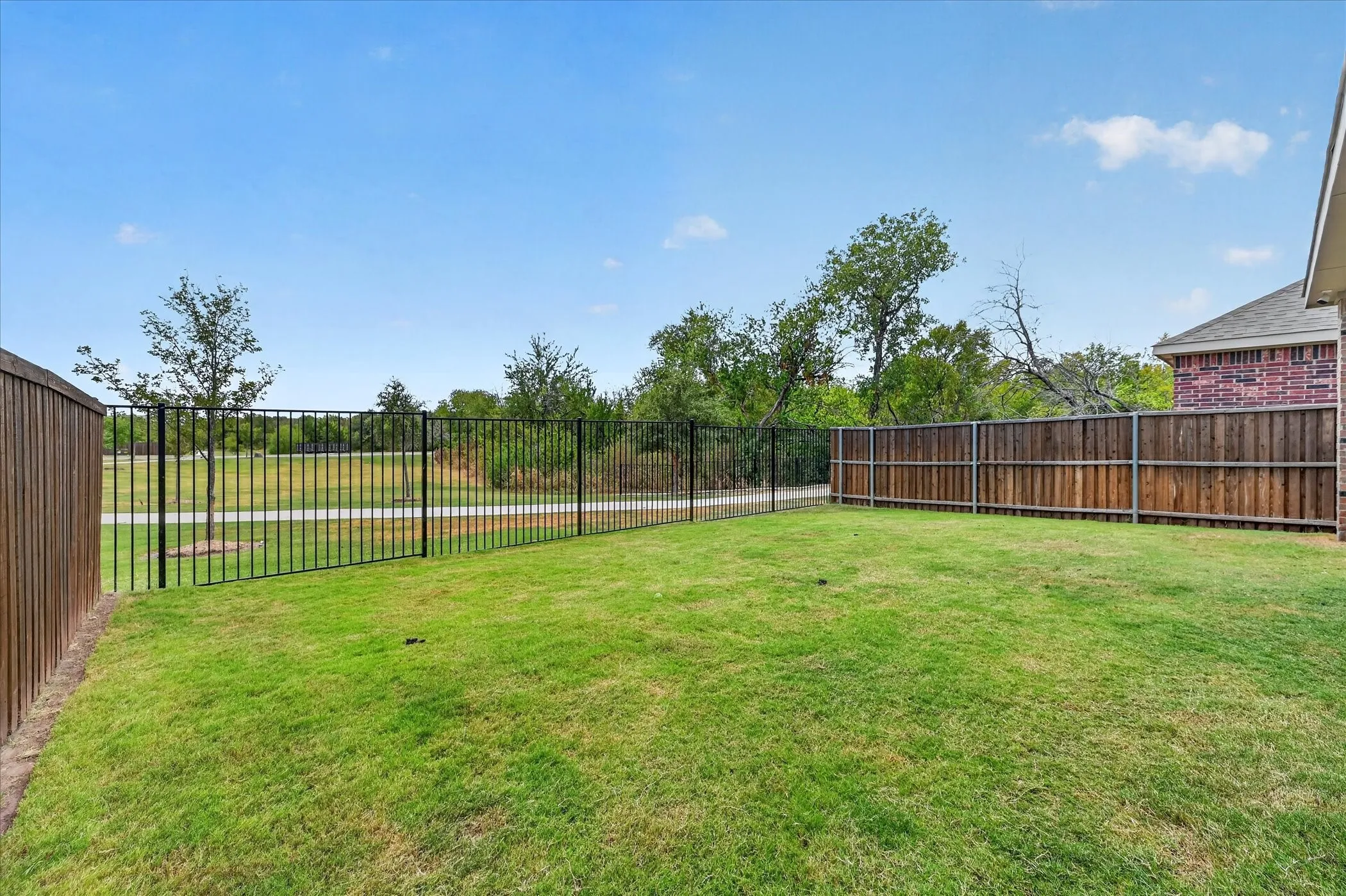 Expansive backyard with a manicured lawn, wood privacy fencing, and black metal fencing