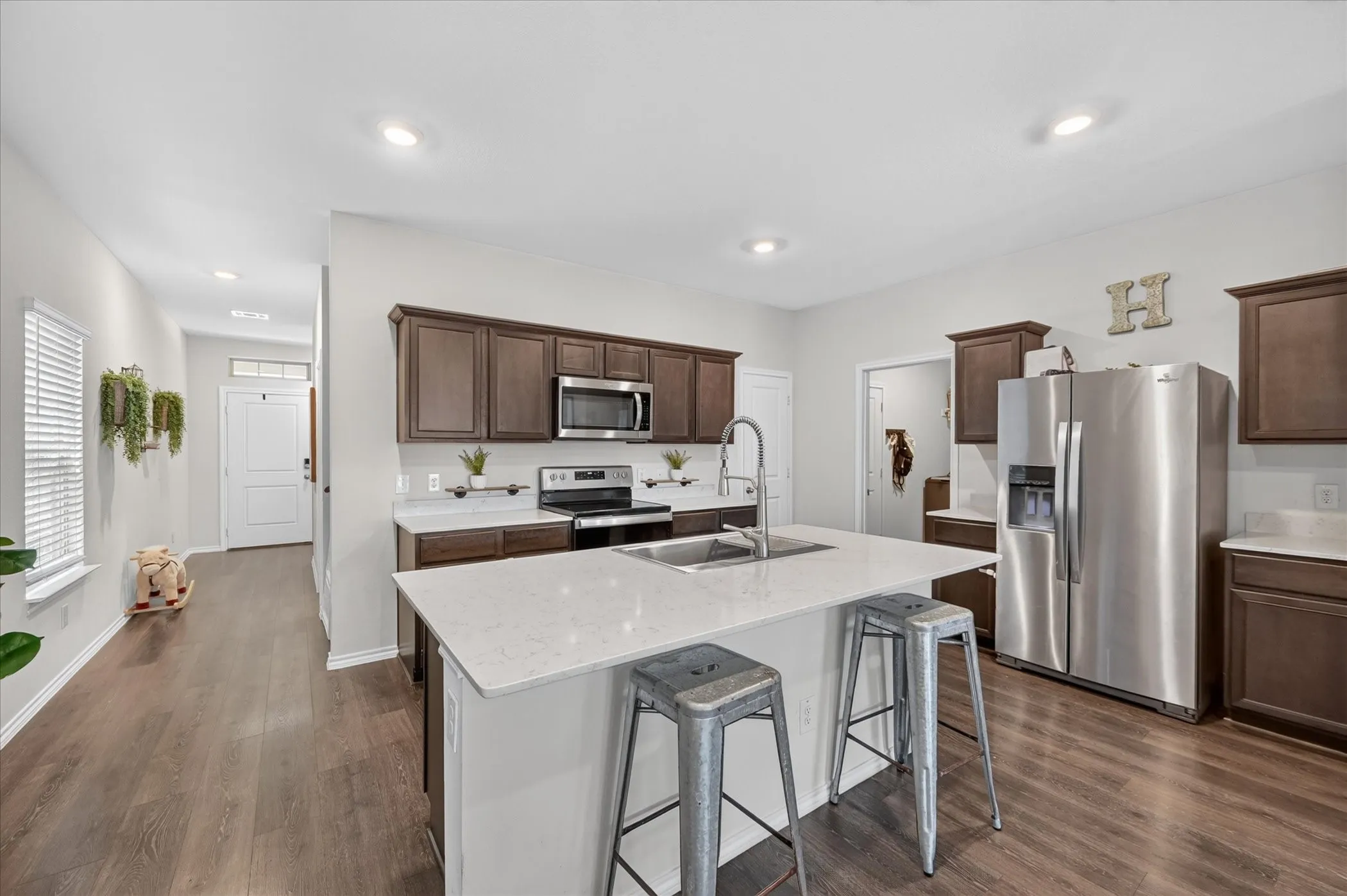 Kitchen featuring a center island with sink, stainless steel appliances, rich wood-finish cabinetry, light countertops, and wood-finish flooring