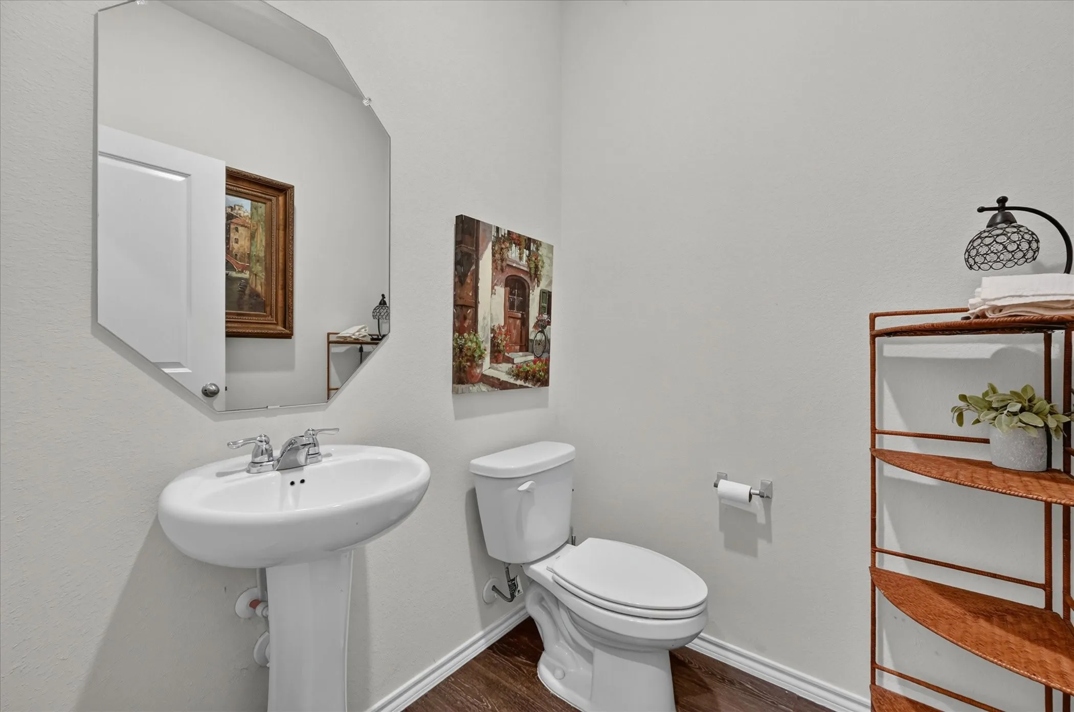 Pedestal sink with chrome fixtures, an octagonal wall mirror, and wood-finish flooring