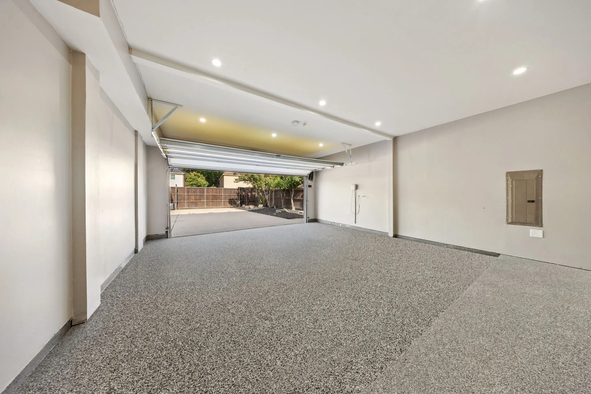 Spacious garage featuring a durable speckled epoxy floor, recessed ceiling lighting, a roll-up door, and painted walls