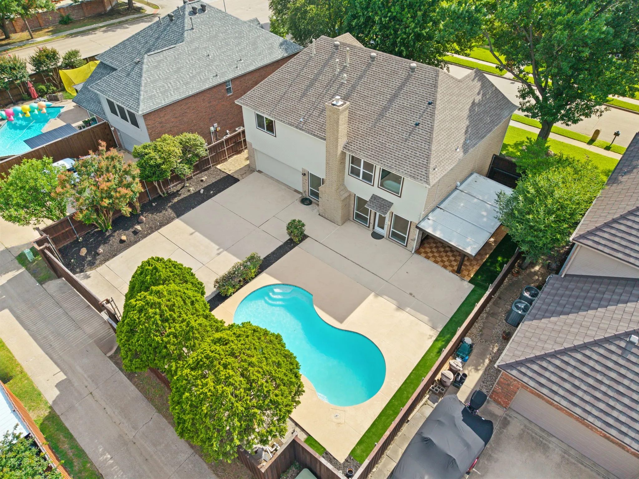 Spacious backyard featuring a kidney-shaped swimming pool, extensive concrete patio, and a covered outdoor living area with patterned tile flooring