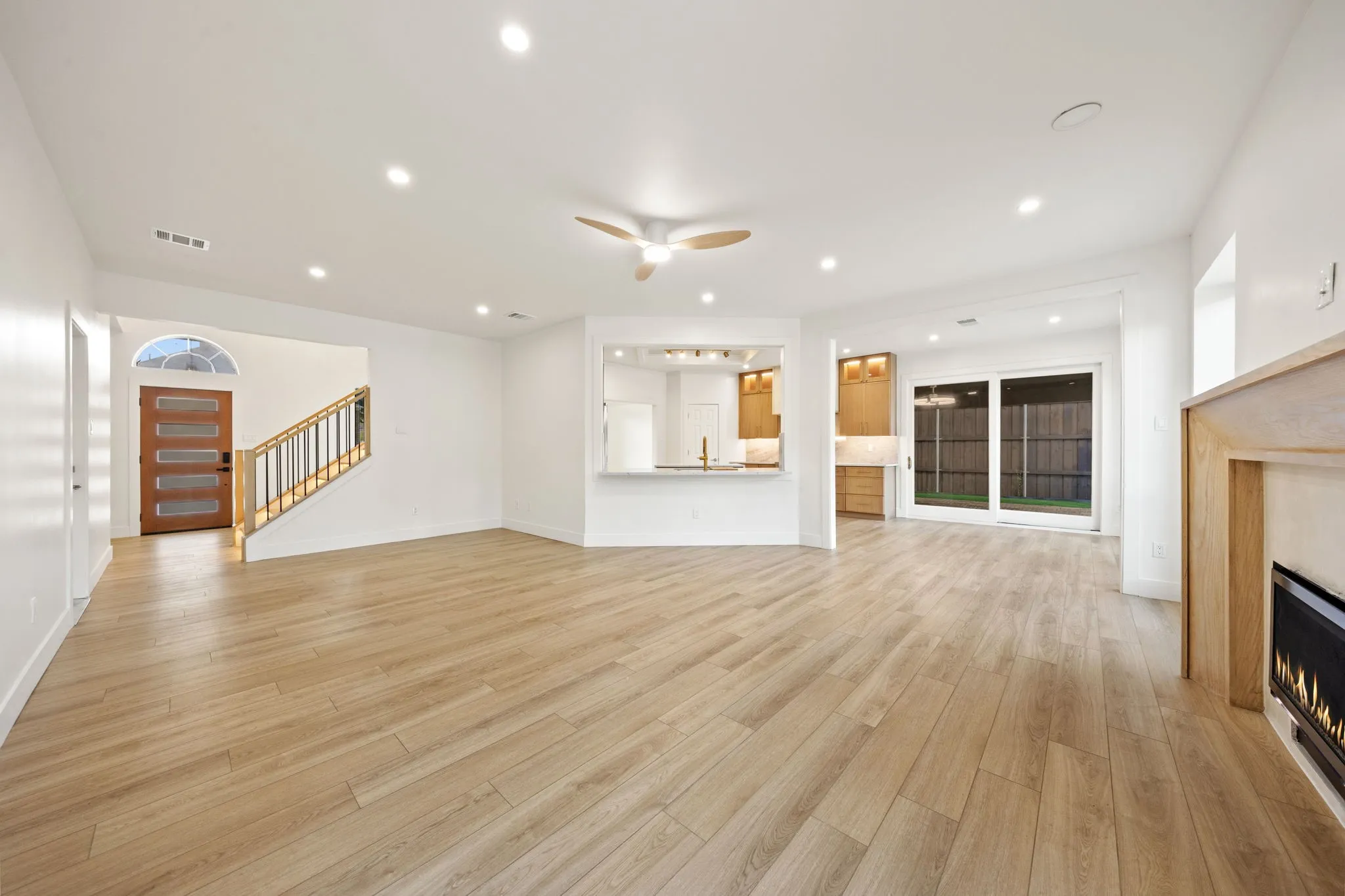 Expansive living area with light wood-finish flooring, recessed lighting, and a modern ceiling fan