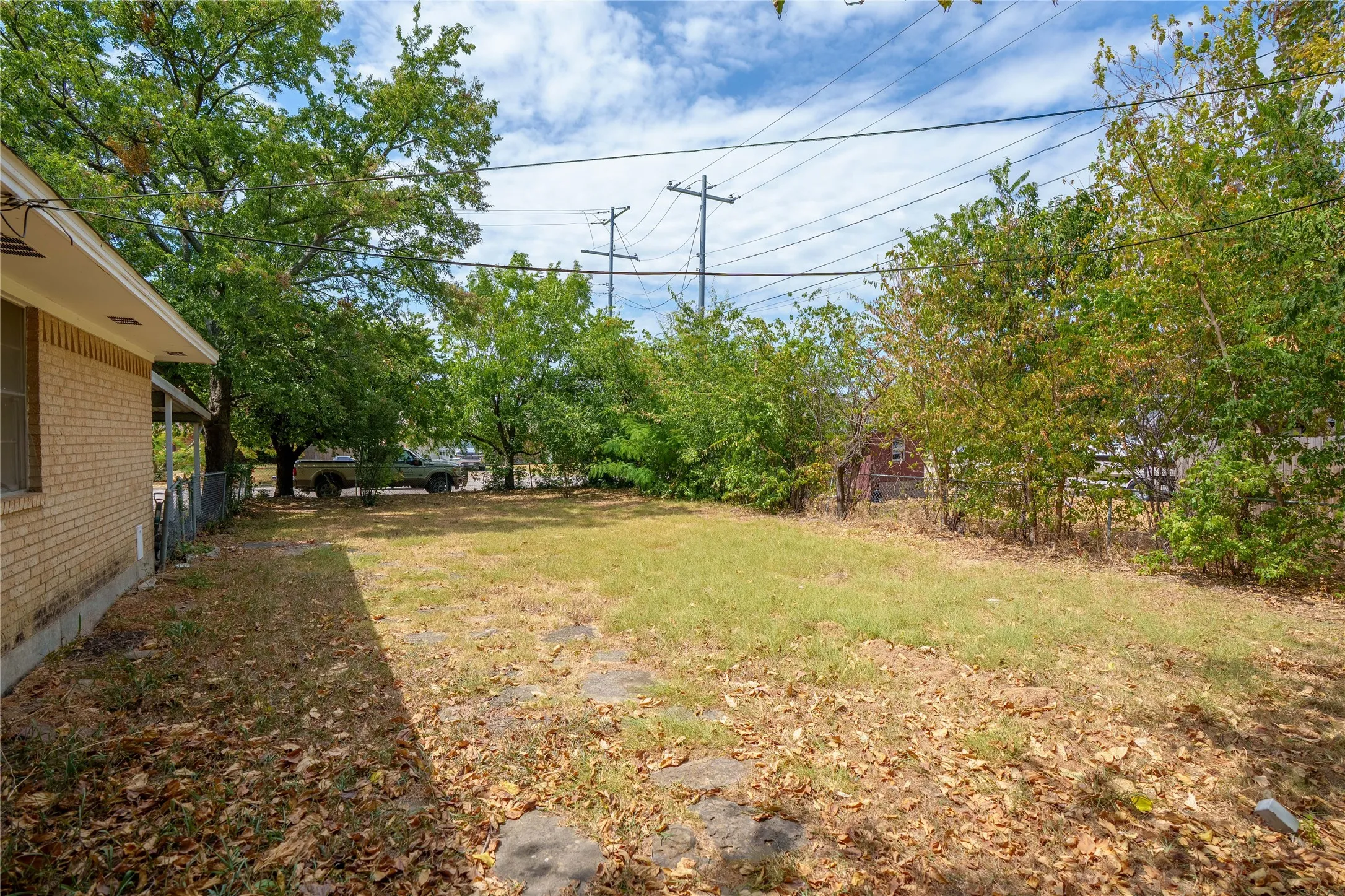Expansive yard space with mature trees, brick exterior, and partial fencing