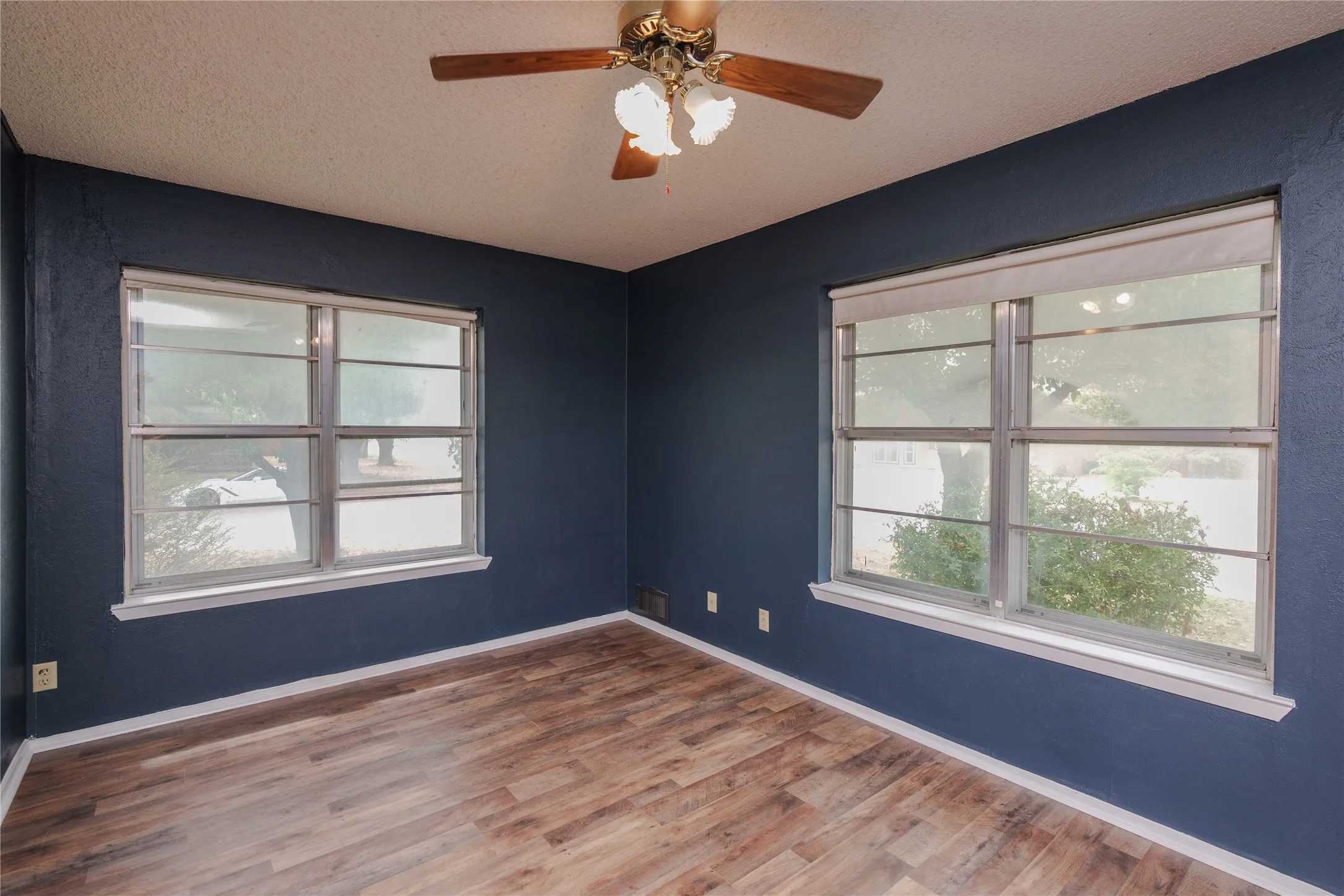 Wood-finish flooring, two window units, and a ceiling fan with integrated lighting