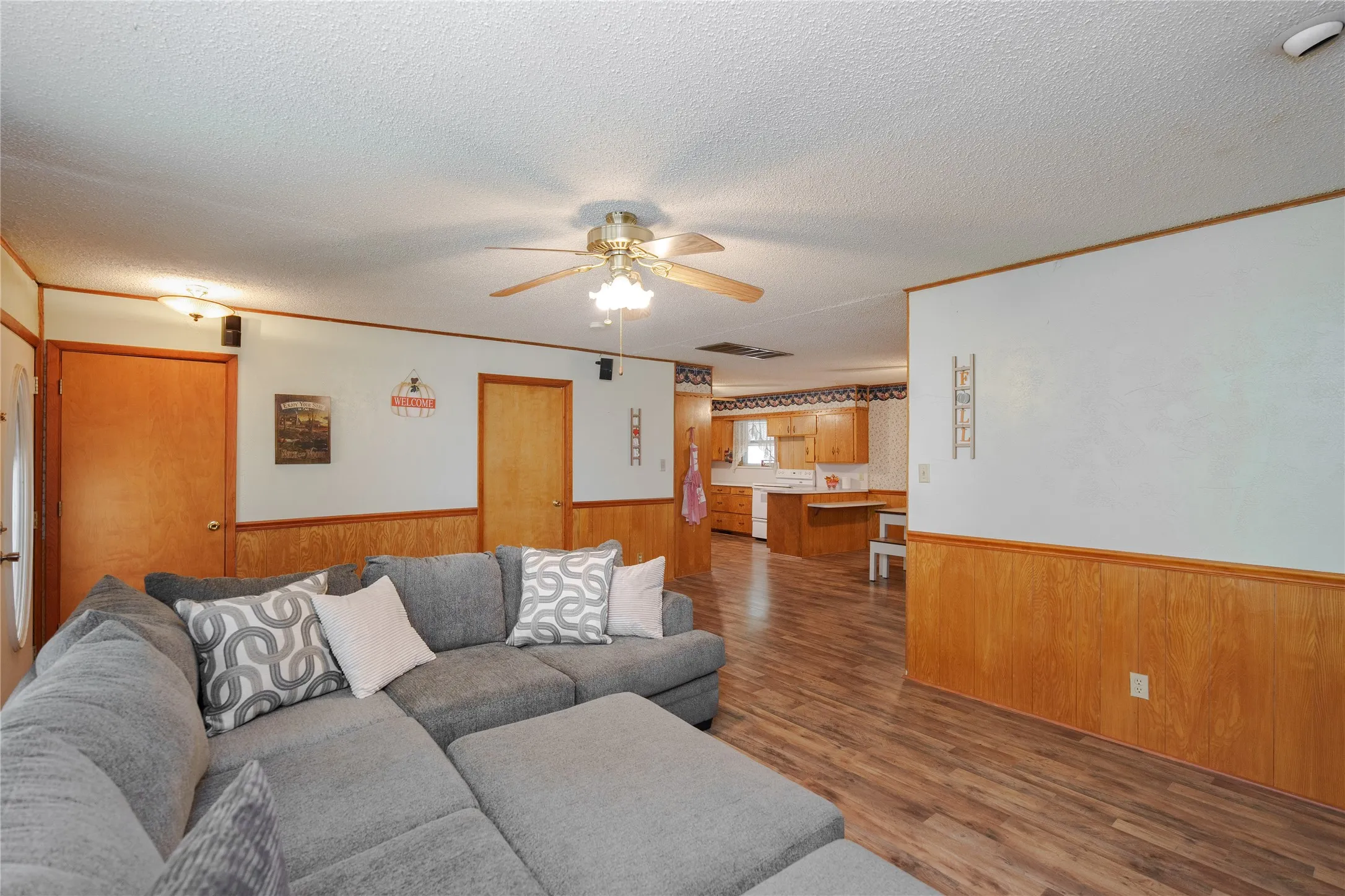 Open-concept living area with wood-finish flooring, wood paneling, and a ceiling fan