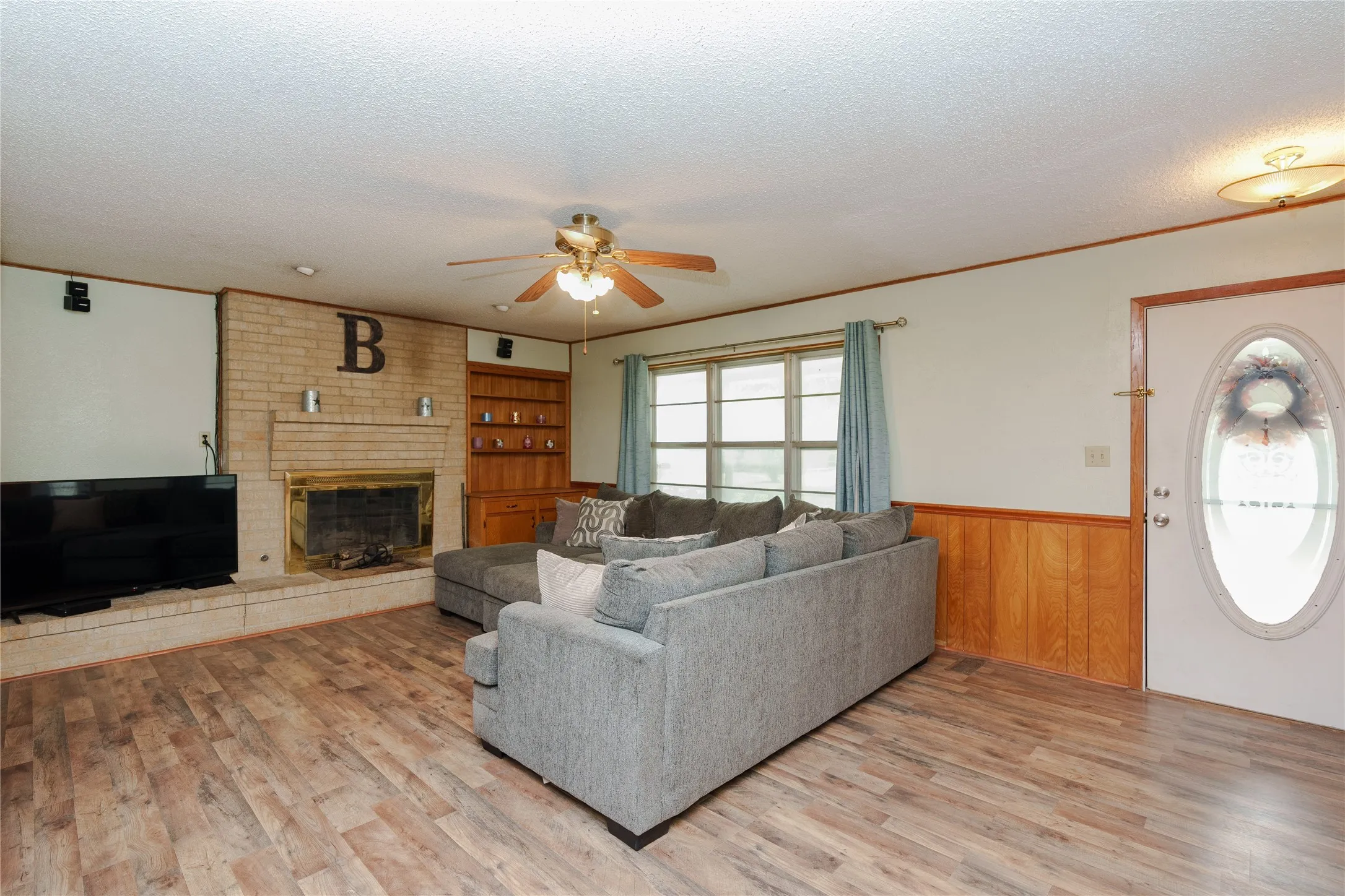 Living area featuring wood-finish flooring, a brick fireplace with a hearth, and built-in shelving