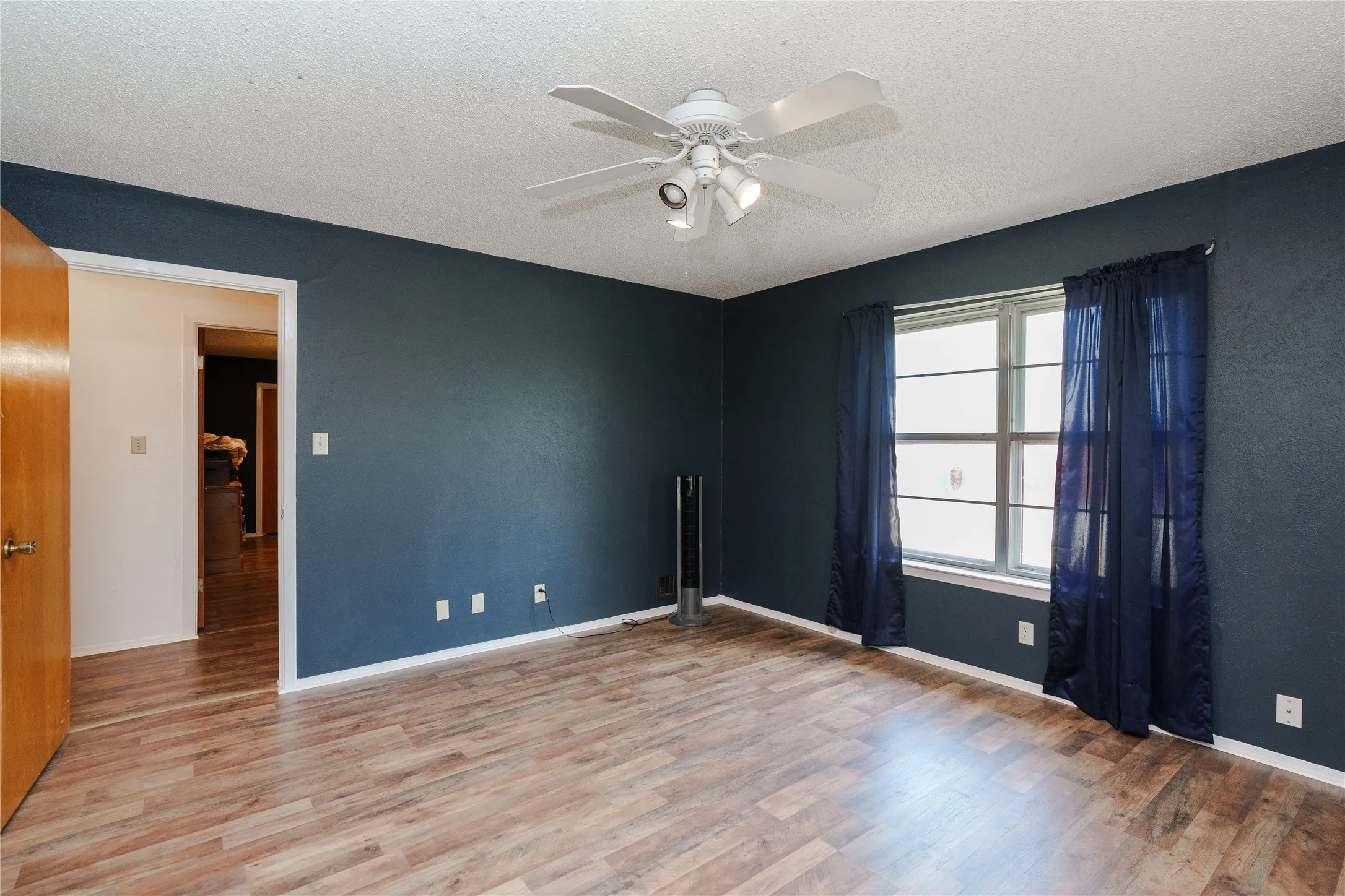 Wood-finish flooring, white ceiling fan with integrated lighting, and a window with white trim